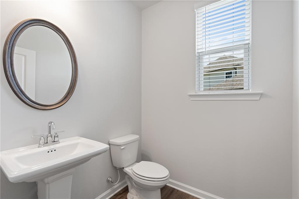 Cozy powder room with pedestal sink, round mirror, and window blinds in Davidson Homes The Hickory A, Winder, Georgia