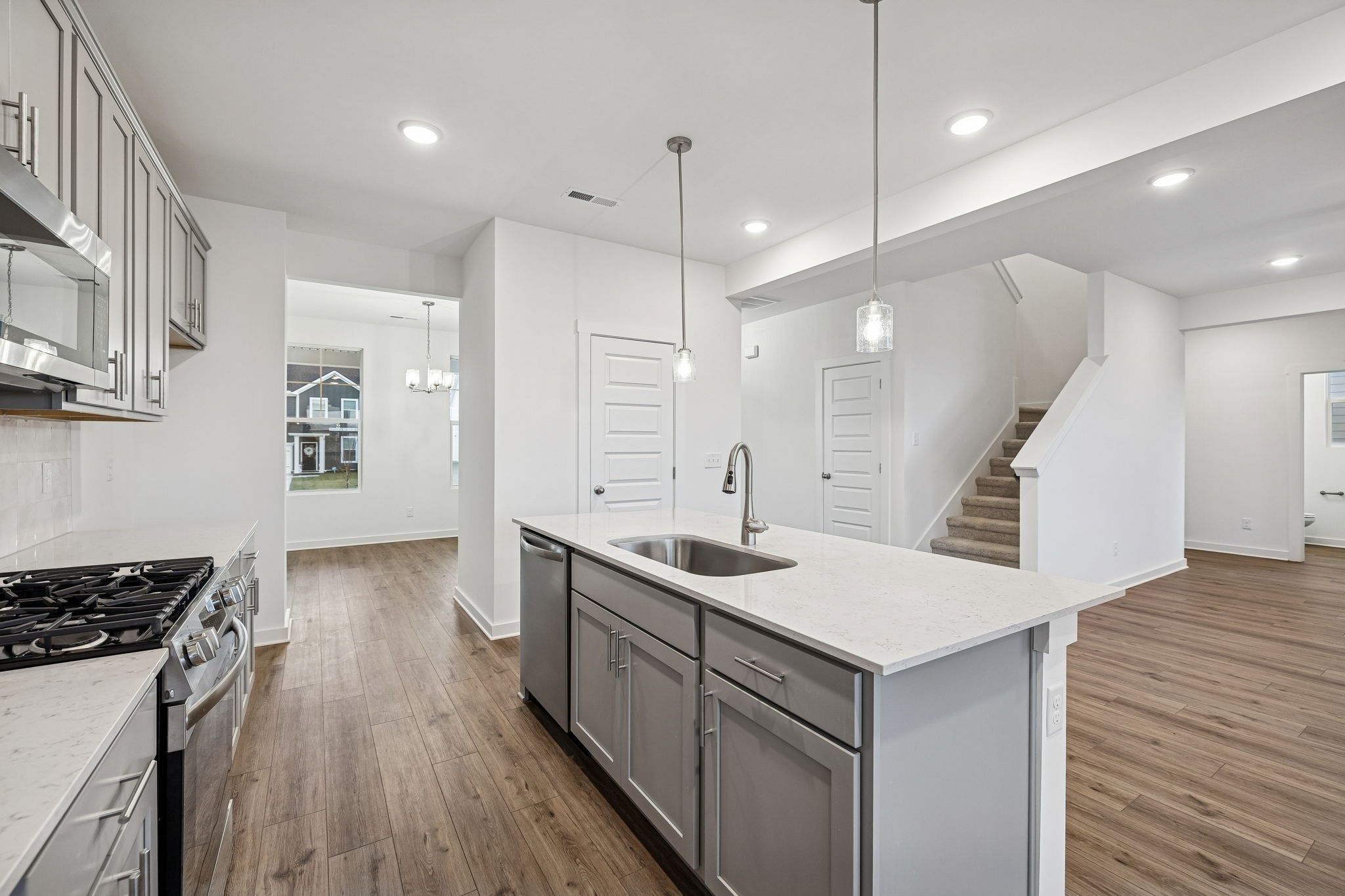 Modern white shaker kitchen with quartz island sink, stainless gas range, and open hardwood floors in Davidson Homes The Willow, Calista Farms, TN