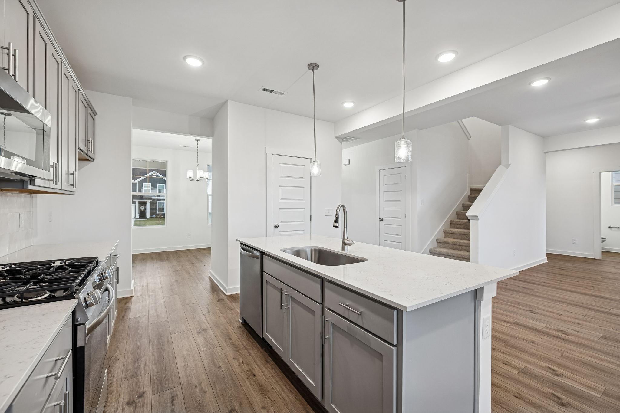 Modern white shaker kitchen with quartz island sink, stainless gas range, and open hardwood floors in Davidson Homes The Willow, Calista Farms, TN