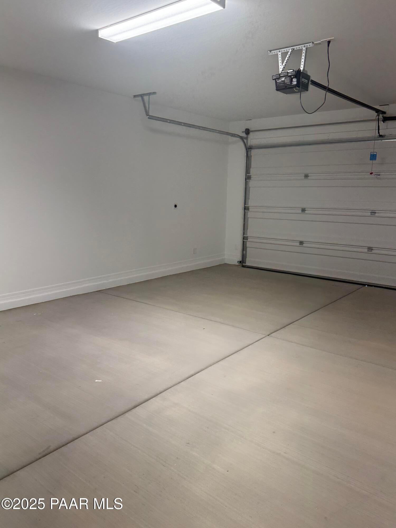 Spacious empty 3-car garage with concrete floor, overhead door, and fluorescent lighting in Davidson Homes The Monarch E, Prescott, Arizona
