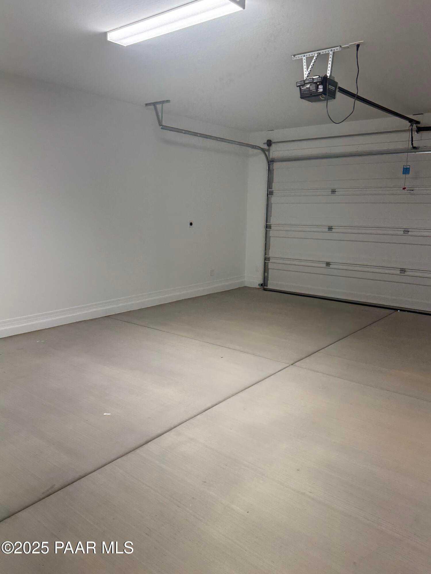 Spacious empty 3-car garage with concrete floor, overhead door, and fluorescent lighting in Davidson Homes The Monarch E, Prescott, Arizona