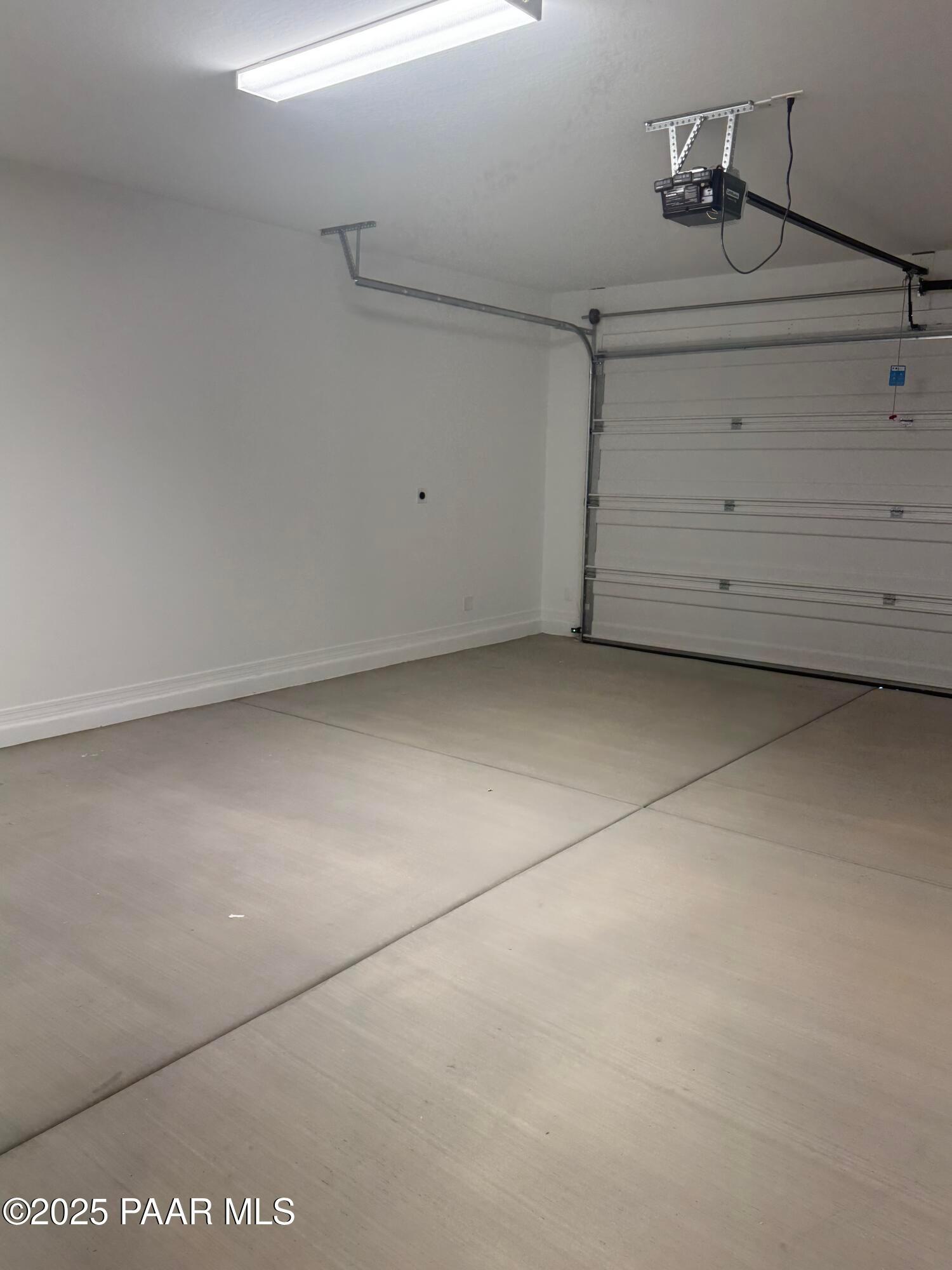 Spacious empty 3-car garage with concrete floor, overhead door, and fluorescent lighting in Davidson Homes The Monarch E, Prescott, Arizona