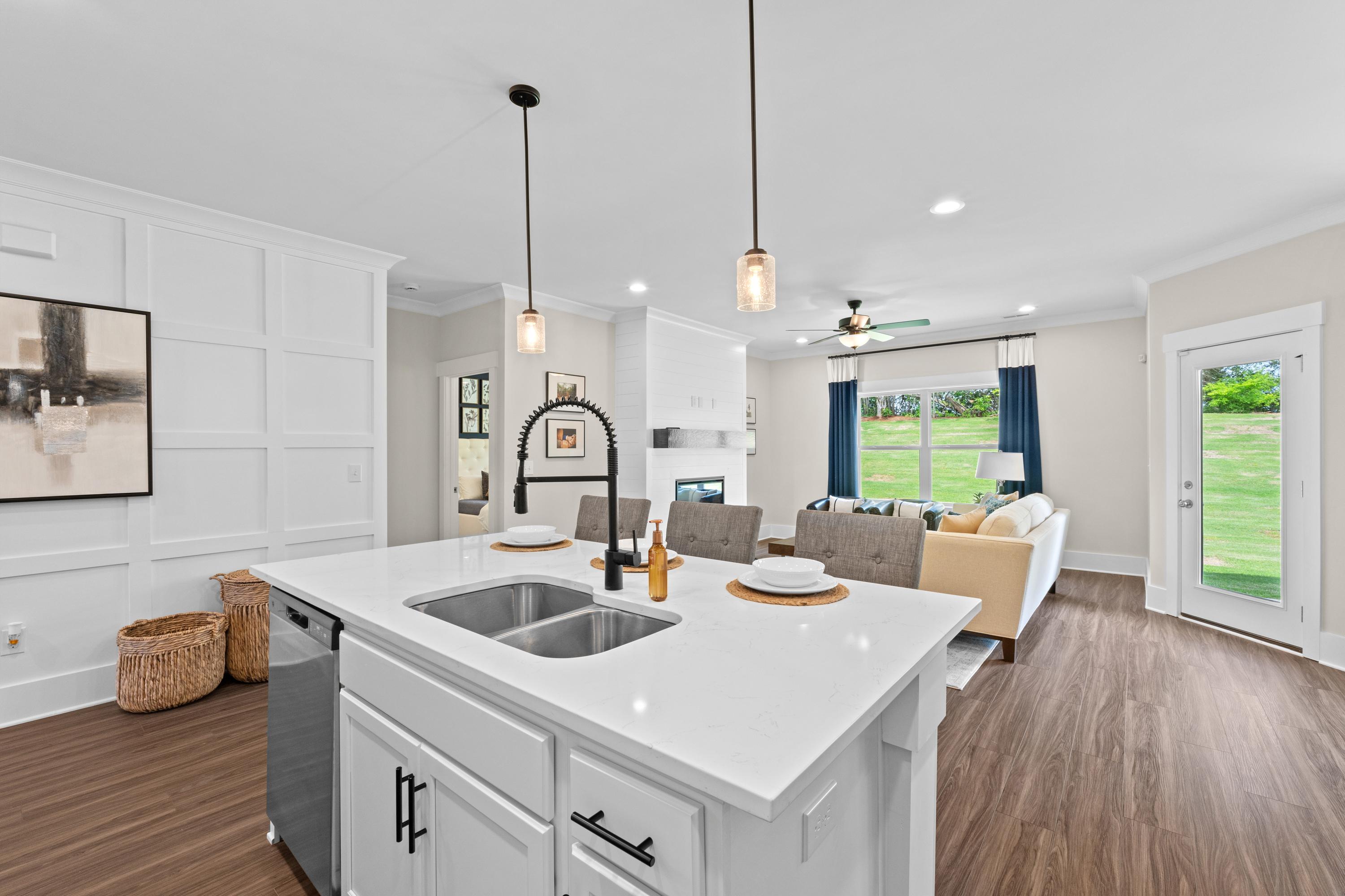 Open-concept kitchen and living room at Ivy Hills in Toney Alabama featuring white island sink, hardwood floors, beige sofa, and French doors to green yard