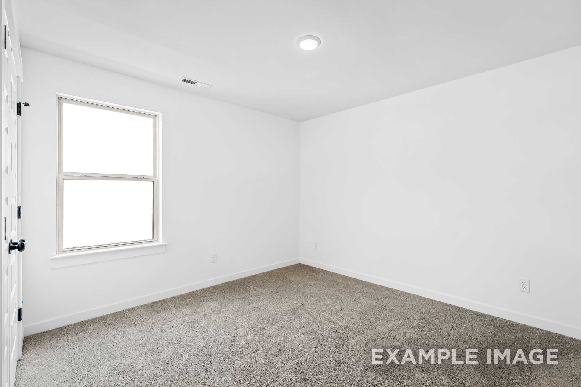 Spacious empty bedroom in The Logan B with white walls, large double-pane window, and gray carpet