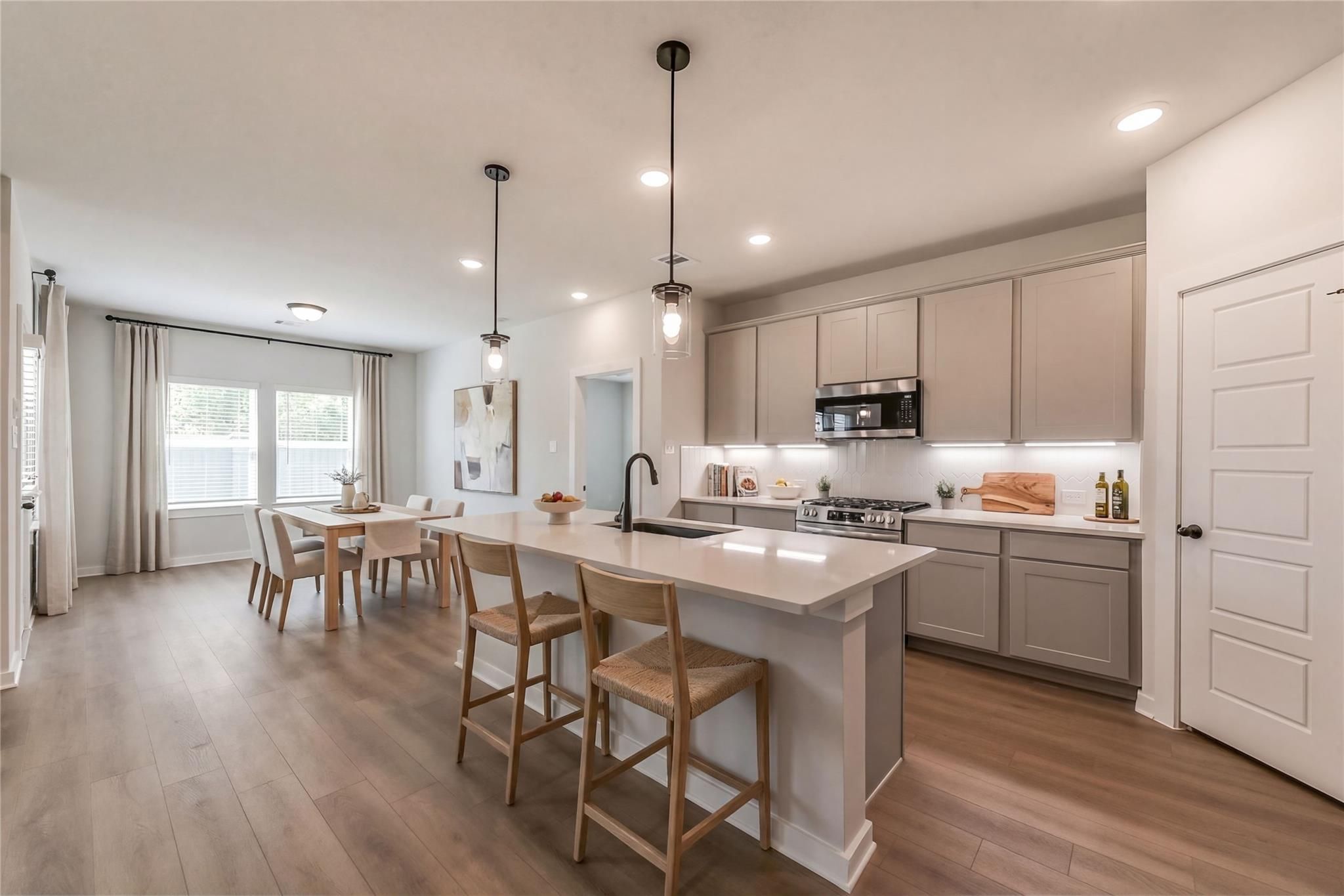 Open-concept kitchen with quartz island, stainless appliances, gray cabinets, and dining nook in The Everett C by Davidson Homes, Crosby, Texas