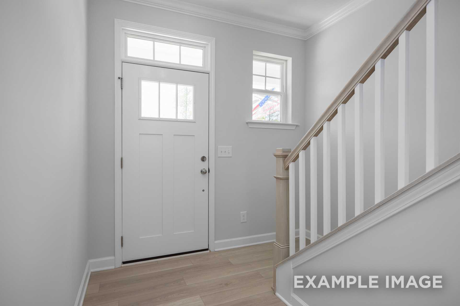Bright entryway in The Gavin C 2-story home with white paneled front door, sidelight window, and oak staircase