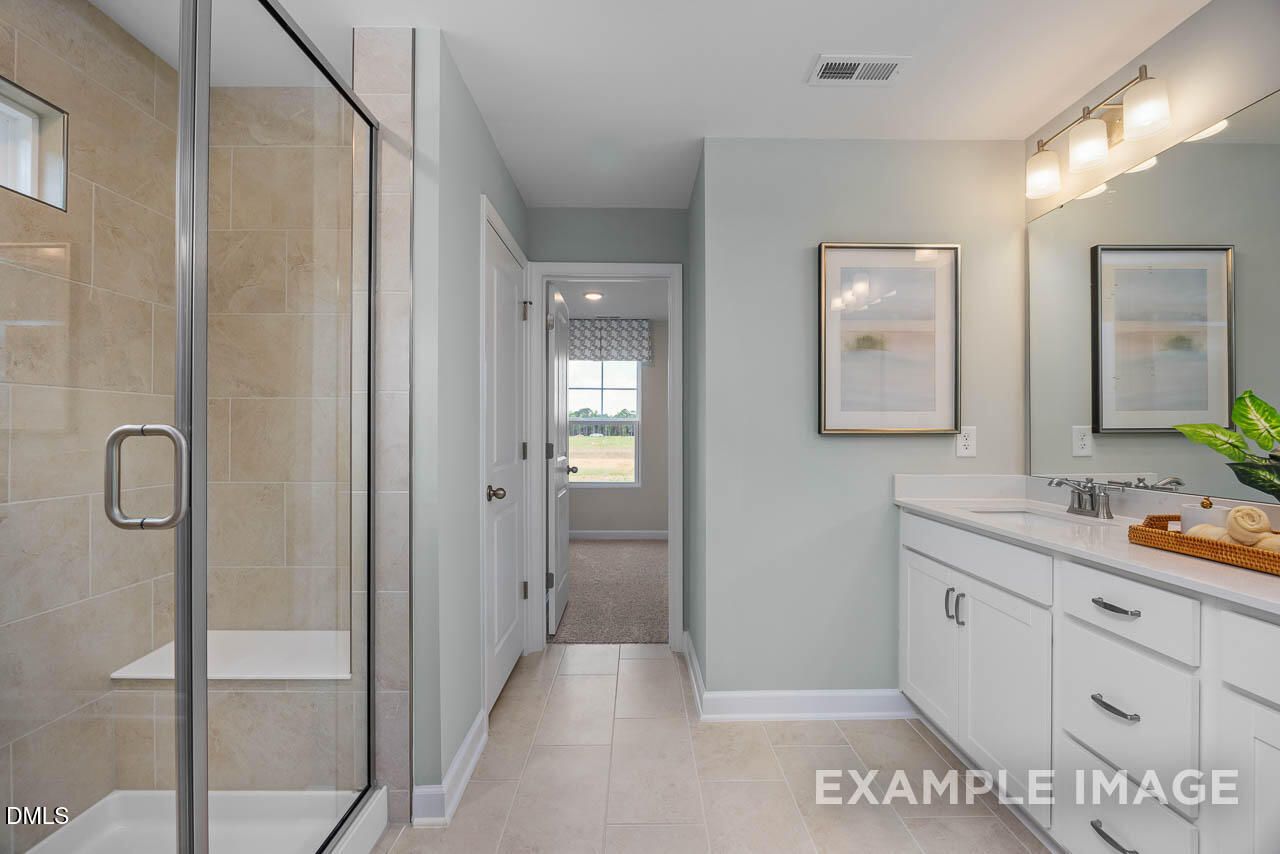 Modern master bathroom with frameless glass shower, double vanity, and hallway to bedroom in Davidson Homes Willow B, Wake Forest, NC