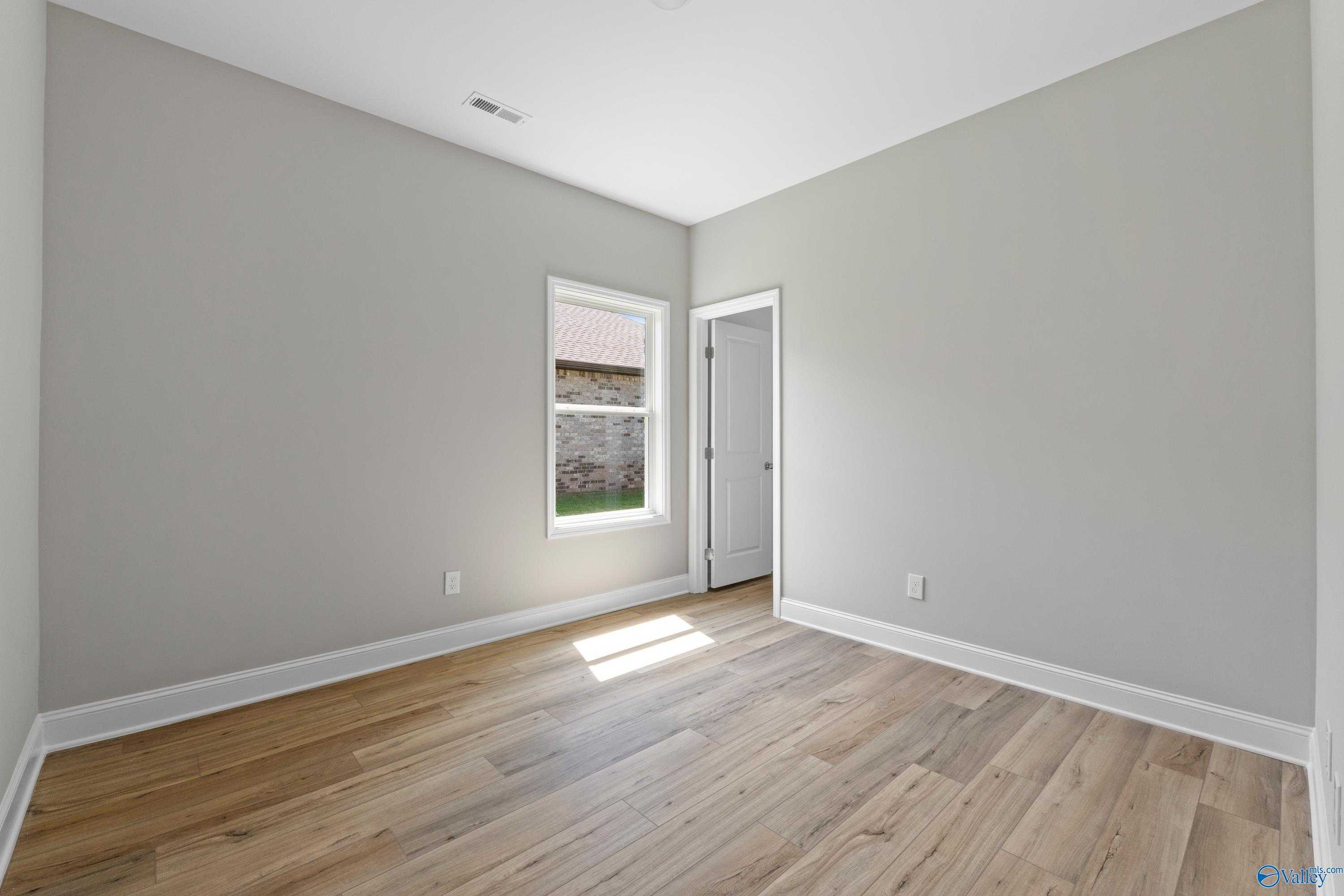 Bright secondary bedroom featuring gray walls, light hardwood floors, and sunny window in Davidson Homes The Daphne C, Athens, Alabama