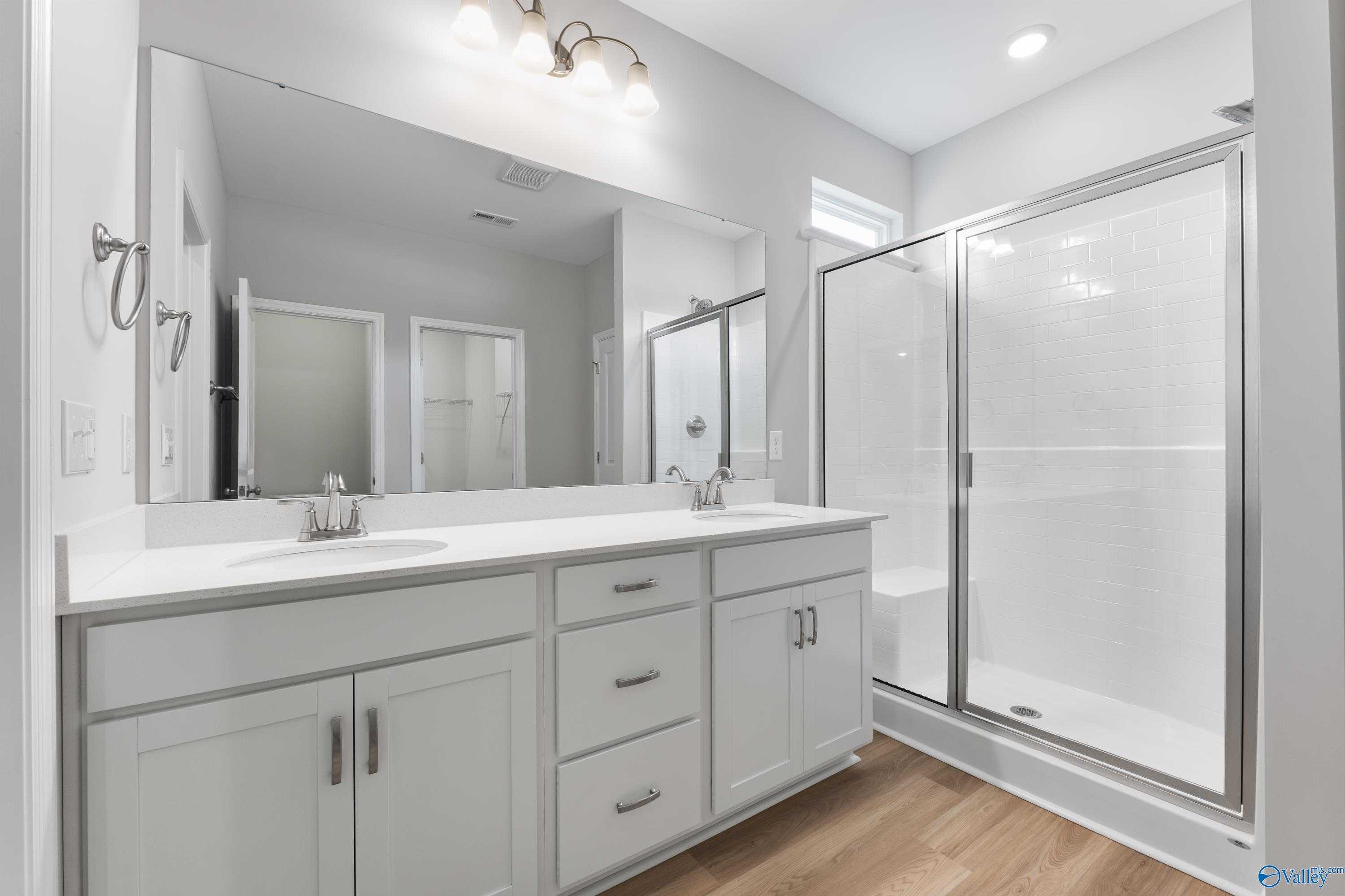 Modern master bathroom featuring double white vanity, frameless glass shower, and subway tile in Davidson Homes The Phoenix, Hazel Green, Alabama