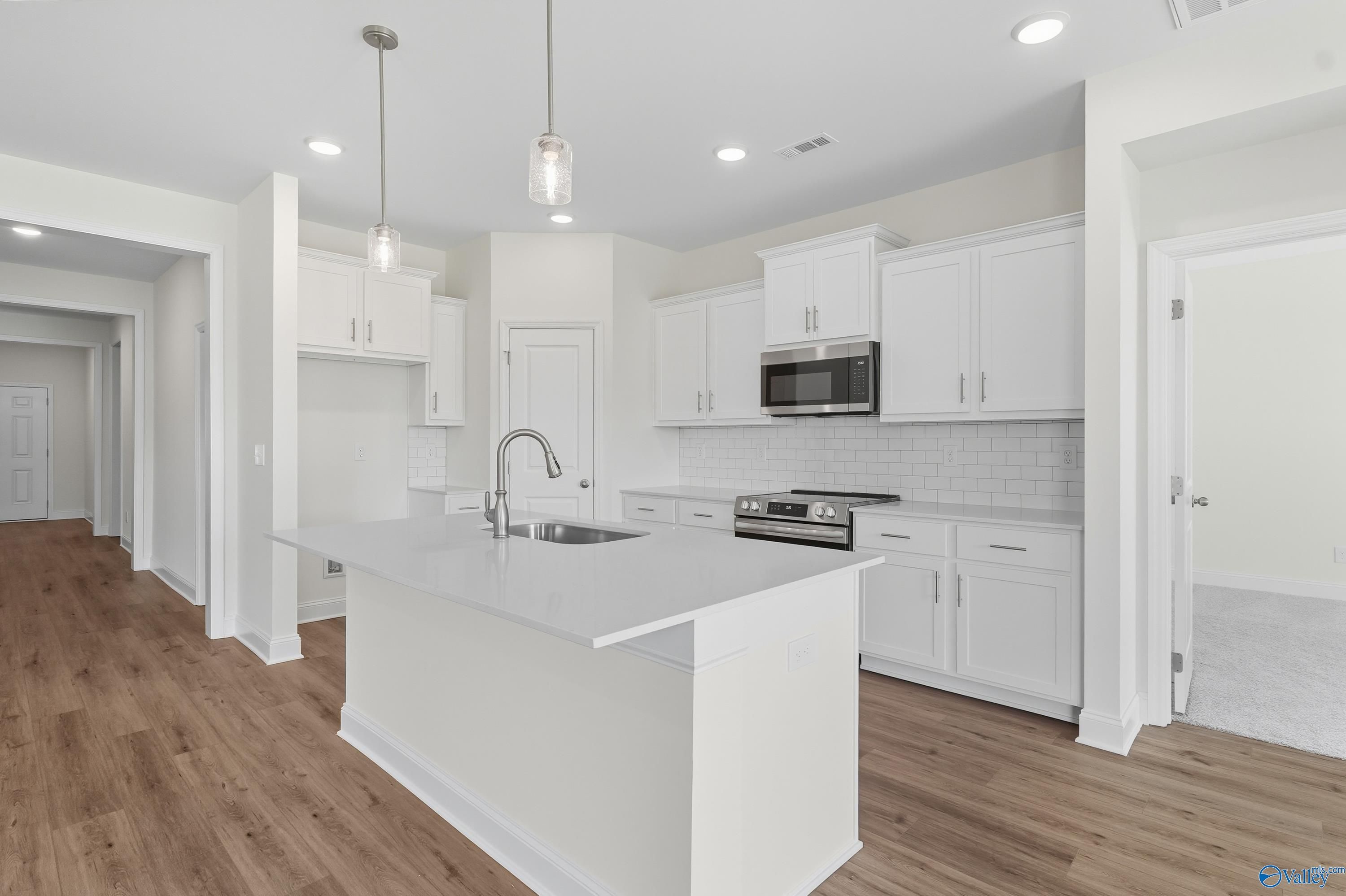 Modern white kitchen island with stainless appliances and hardwood floors in Davidson Homes The Everett, Meridianville, Alabama
