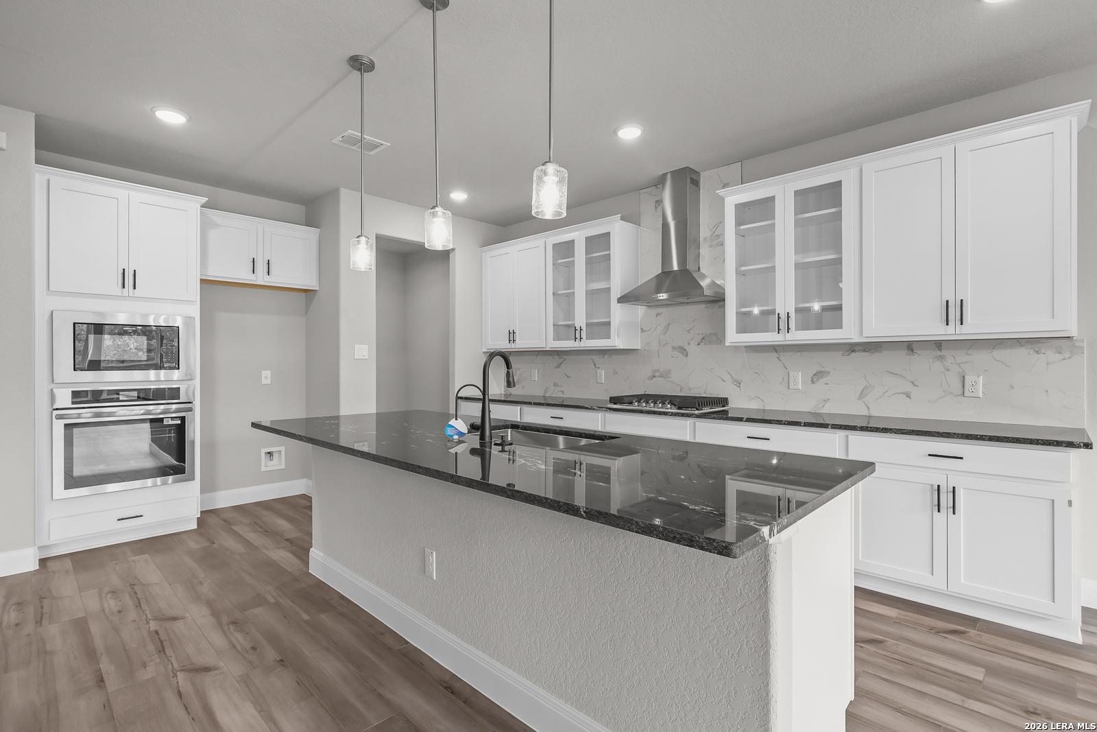 Modern kitchen with white cabinets, black granite island, stainless steel appliances, and pendant lights in Davidson Homes Belmont H, Castroville TX