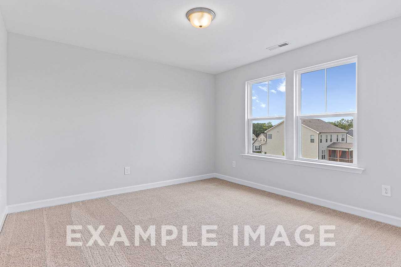 Spacious empty bedroom in The Willow C home design with gray walls, beige carpet, large windows overlooking neighborhood
