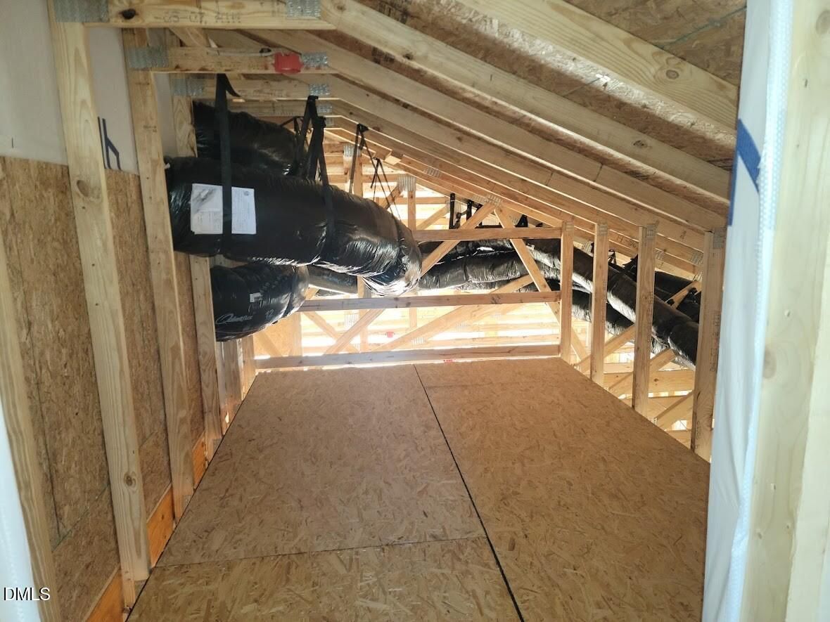 Unfinished attic with exposed wooden rafters, hanging HVAC ducts, and plywood flooring in Davidson Homes Ashport G, Angier, NC