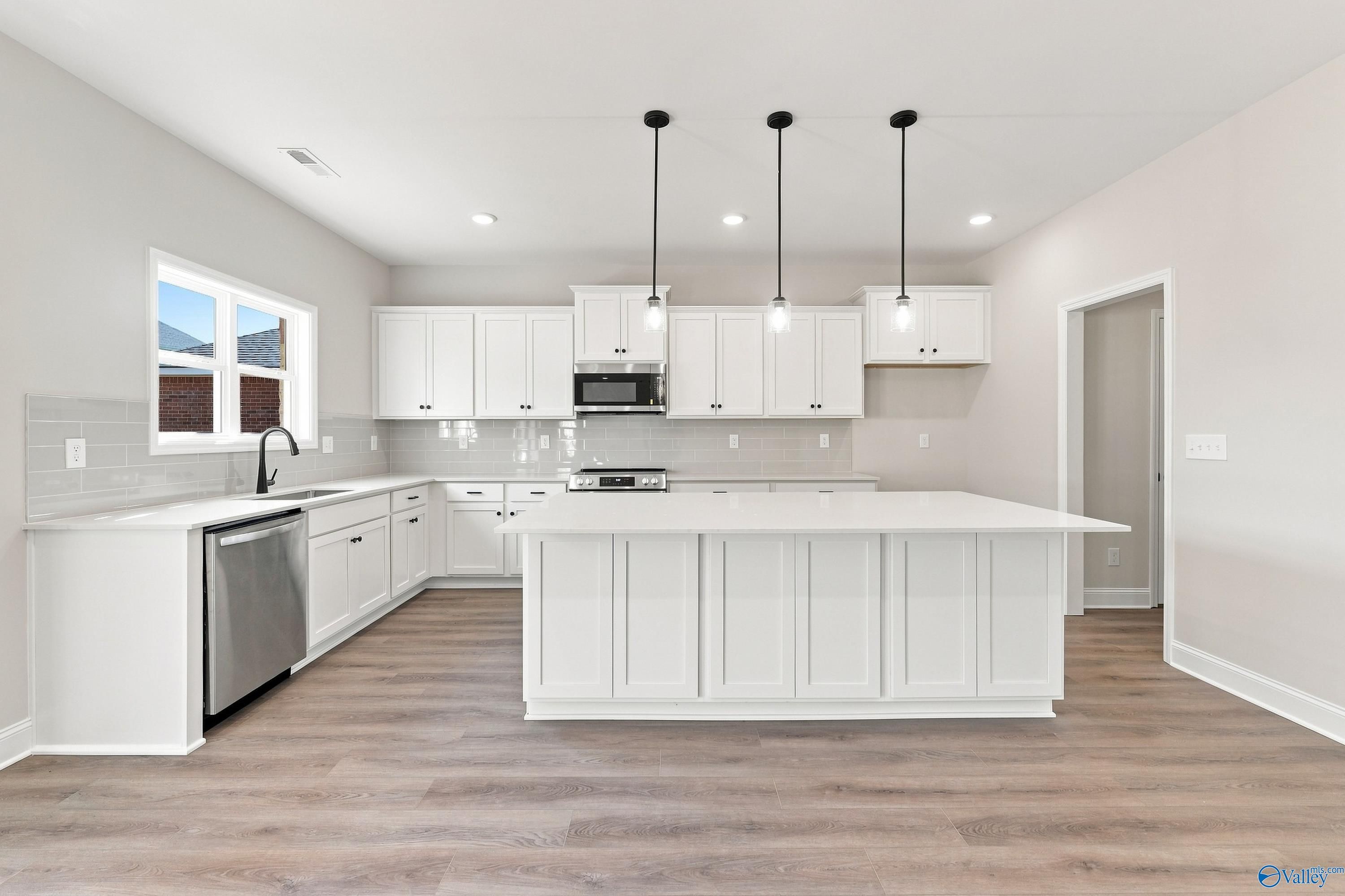 White kitchen with large island, pendant lights, and stainless appliances in Davidson Homes The Chelsea B, New Market, Alabama