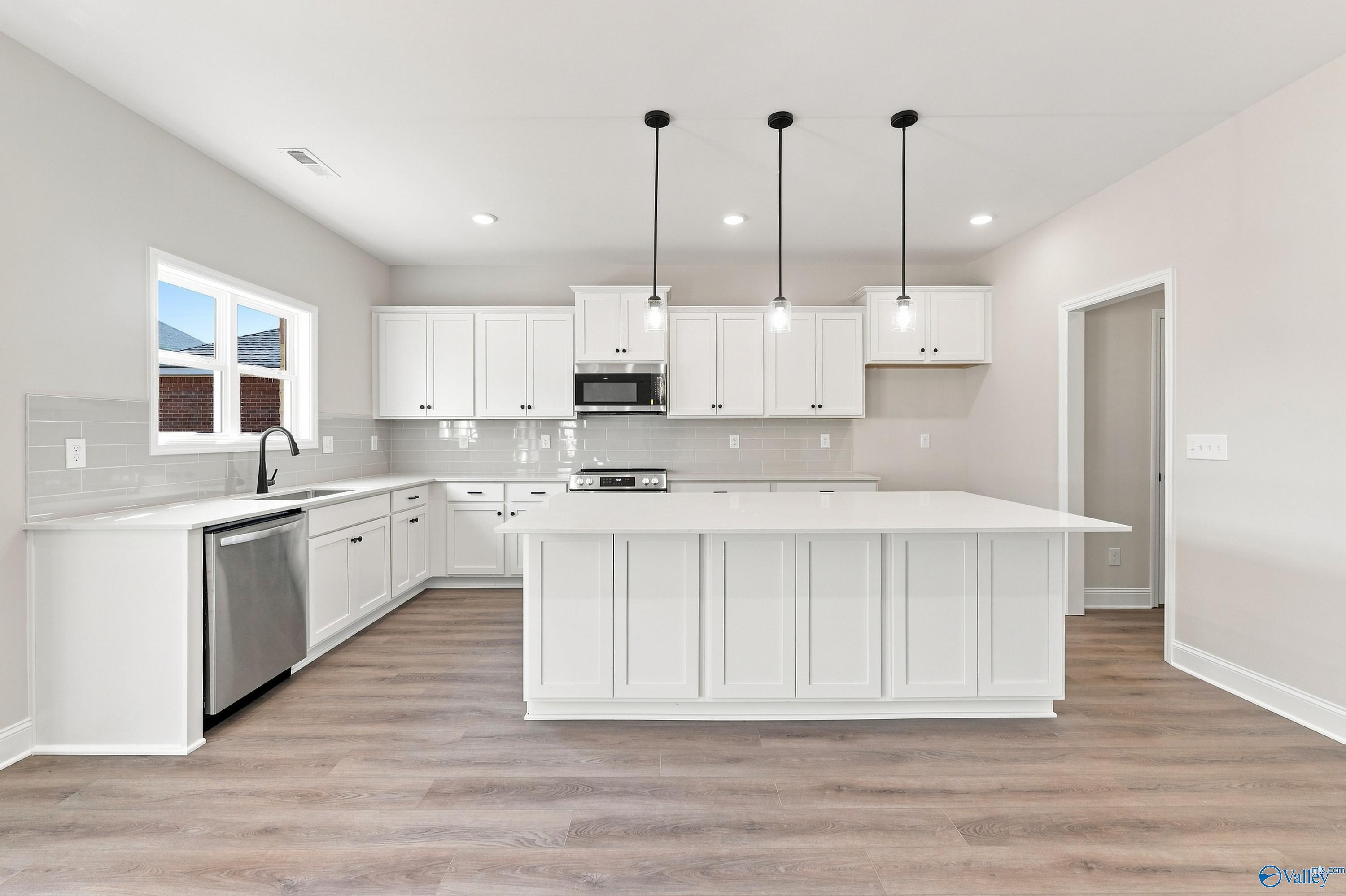 White kitchen with large island, pendant lights, and stainless appliances in Davidson Homes The Chelsea B, New Market, Alabama