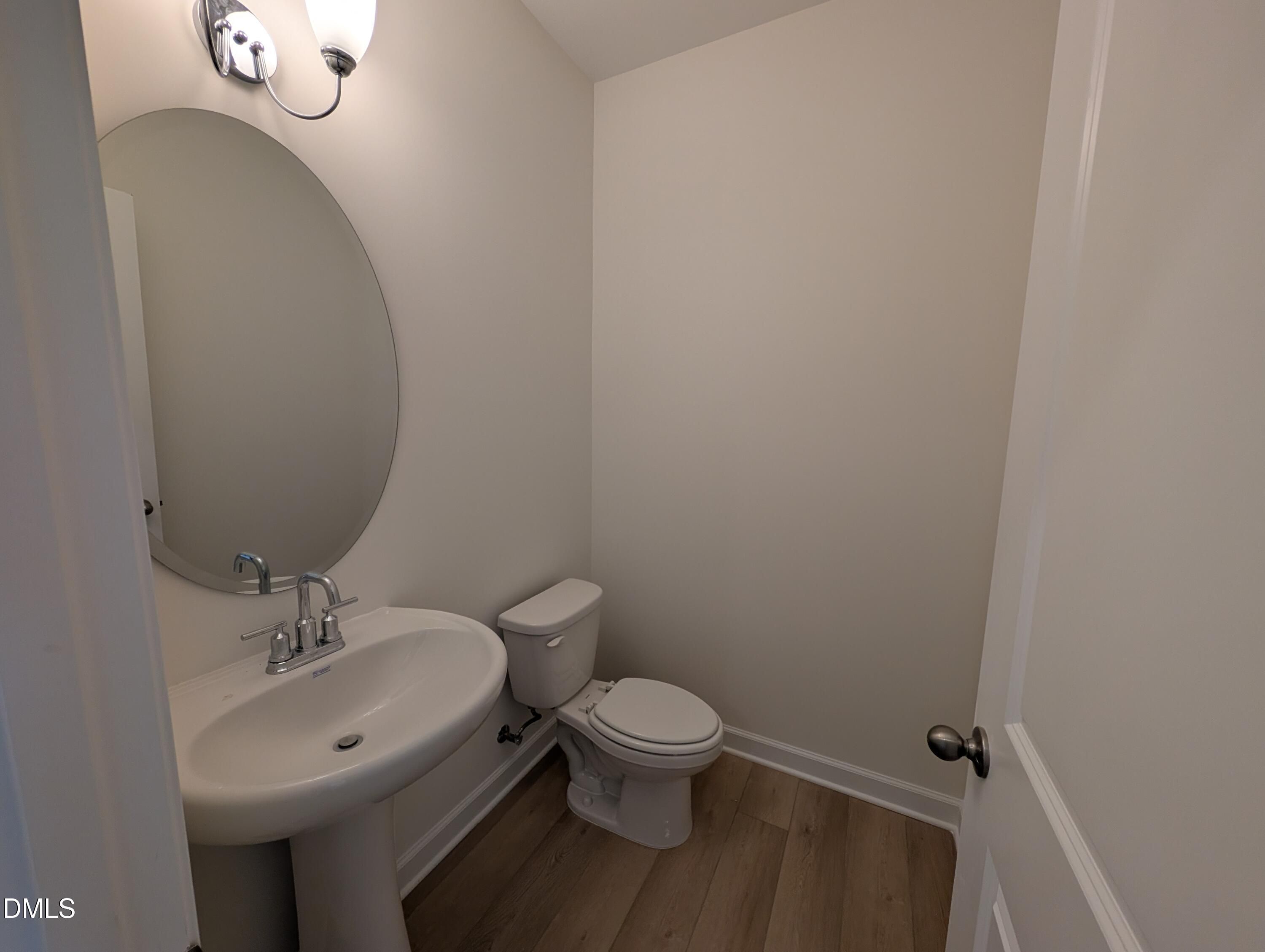 Powder room with pedestal sink, oval mirror, and wood-look flooring in Davidson Homes Magnolia A, Wendell Ridge, NC