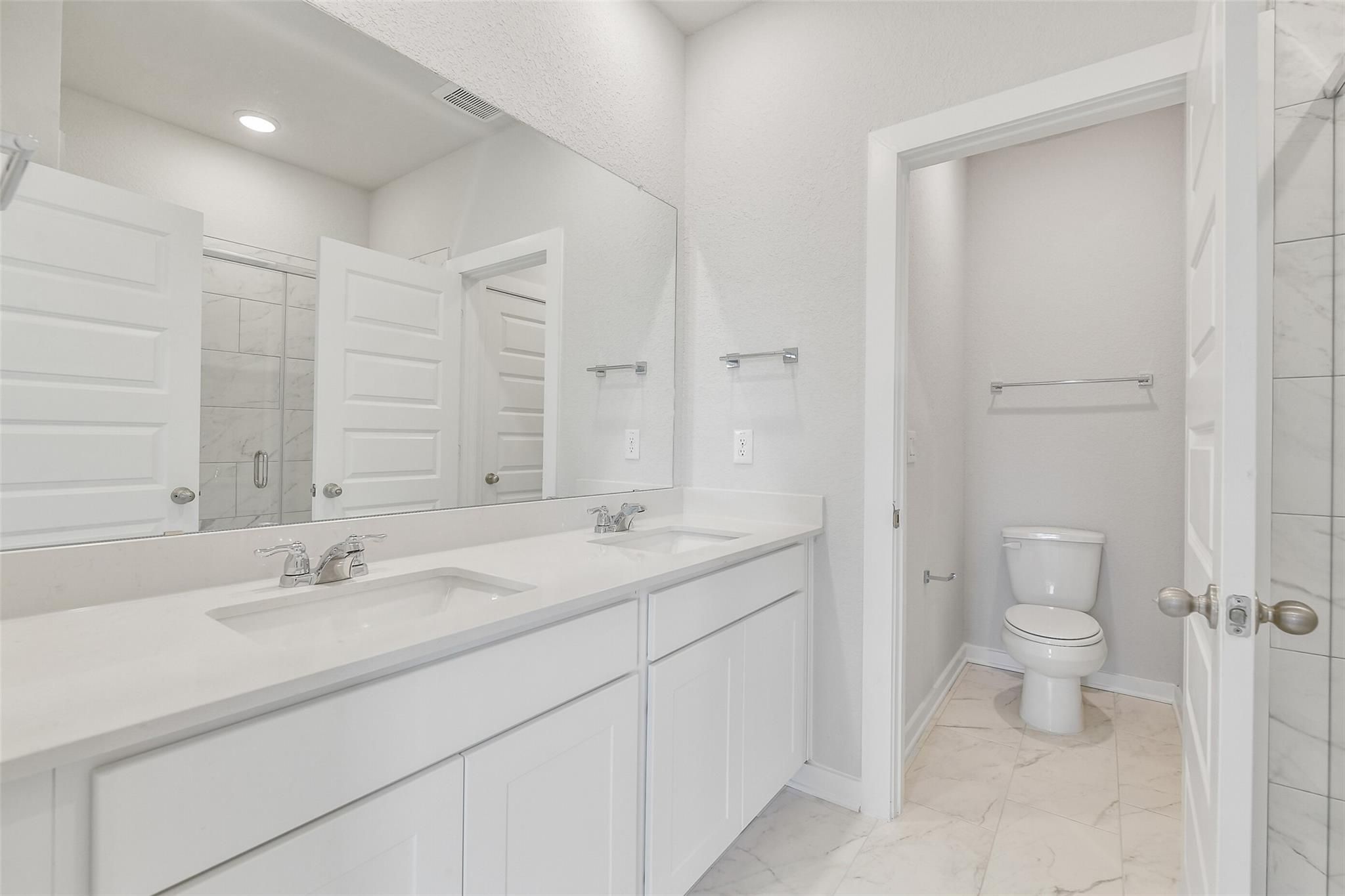 Elegant master bathroom with double white vanity, quartz counters, large mirror, and separate toilet in Davidson Homes The Colorado G, Magnolia, Texas