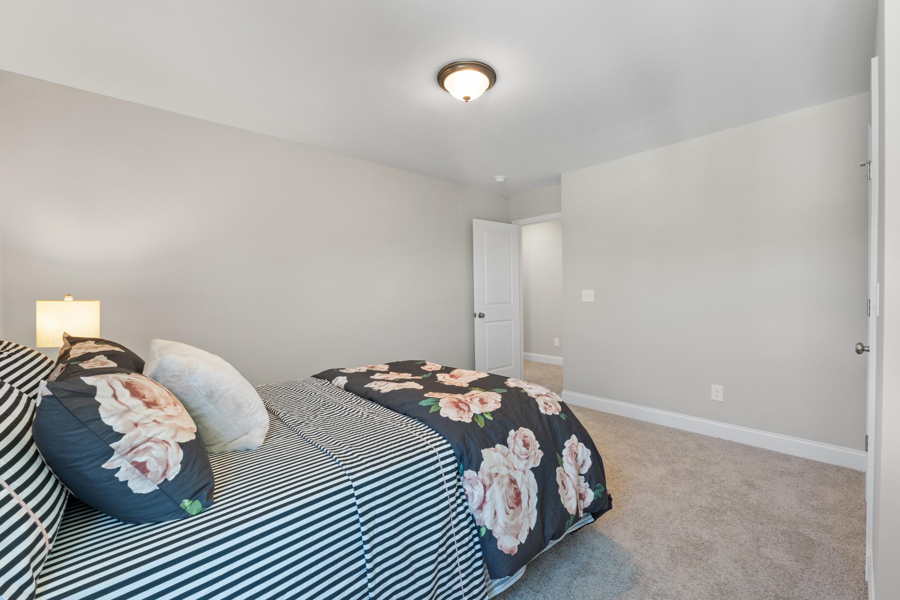 Cozy master bedroom in The Haven D featuring floral rose duvet, striped sheets, nightstand lamp, and gray walls