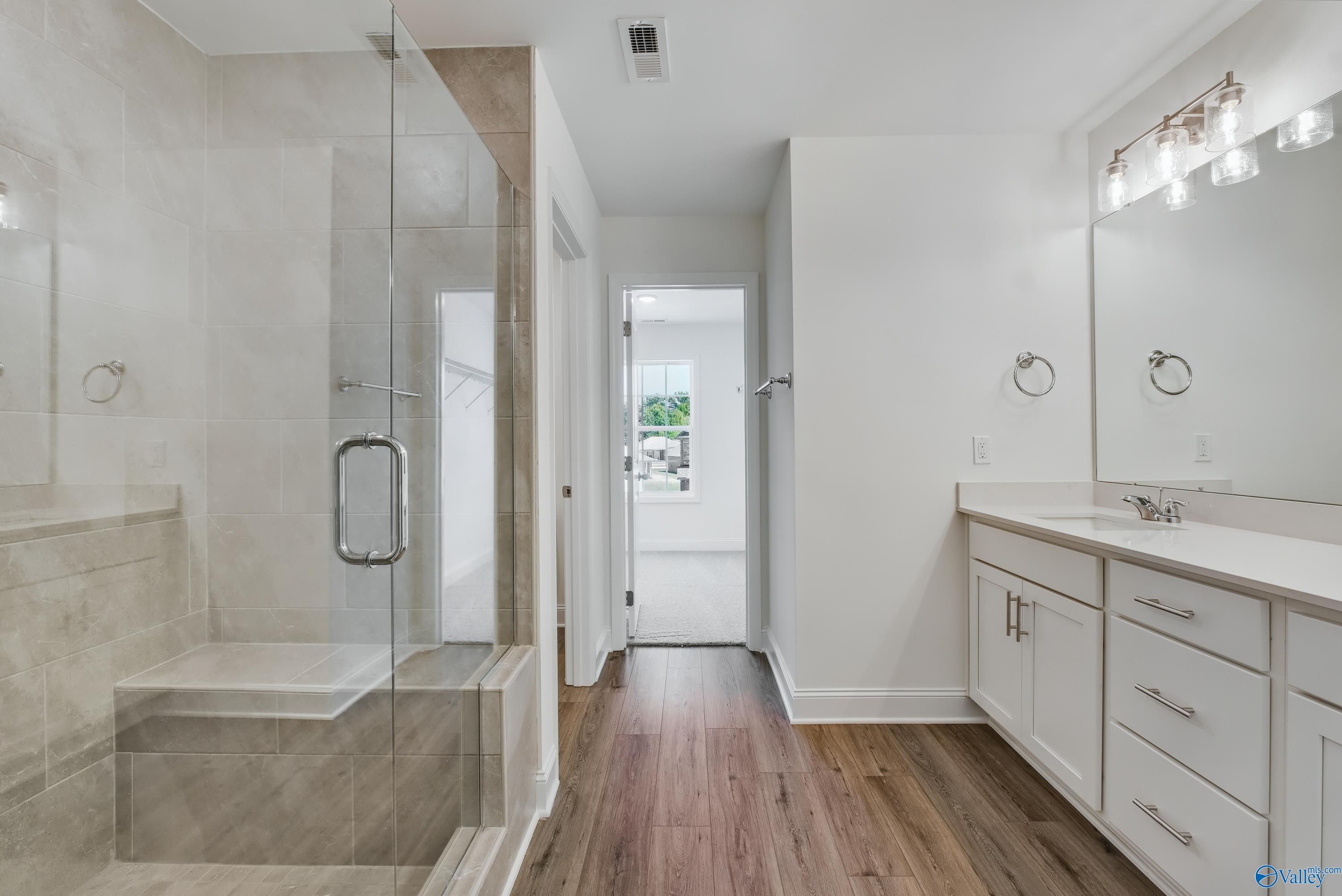 Modern master bathroom featuring frameless glass shower, double white vanity, and hardwood floors in Davidson Homes The Shelby A, Arab, Alabama