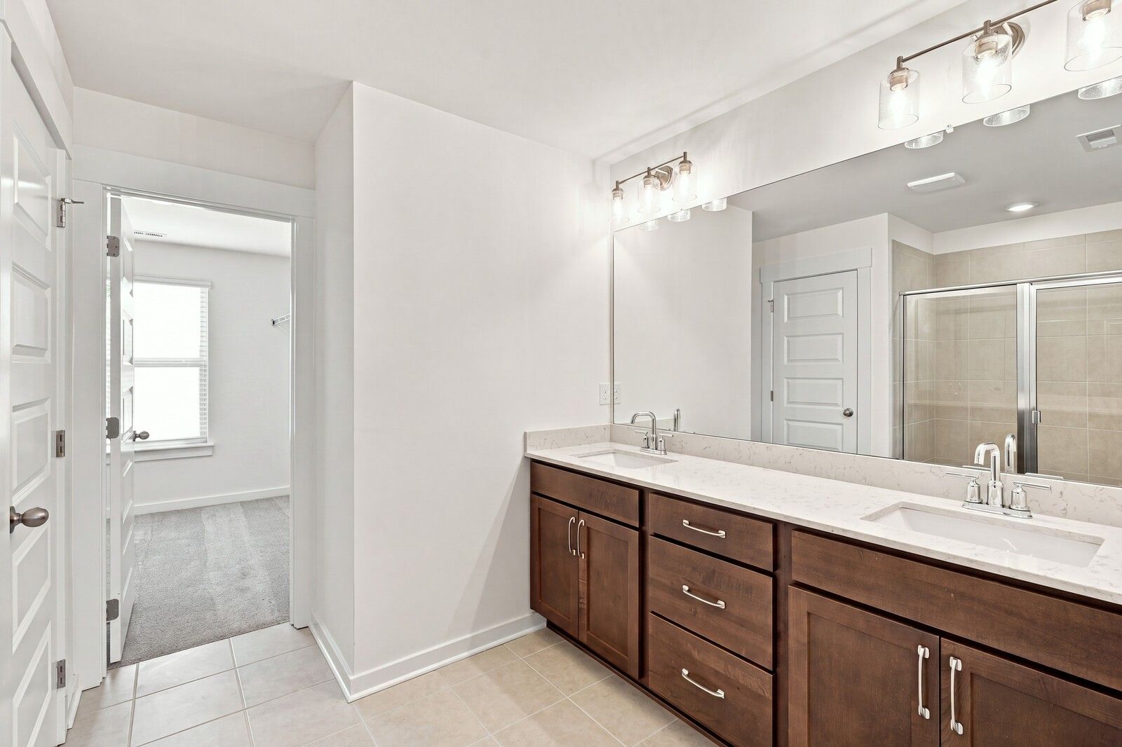 Double vanity bathroom with dark wood cabinets, quartz countertops, and walk-in tiled shower in Davidson Homes The Willow C plan