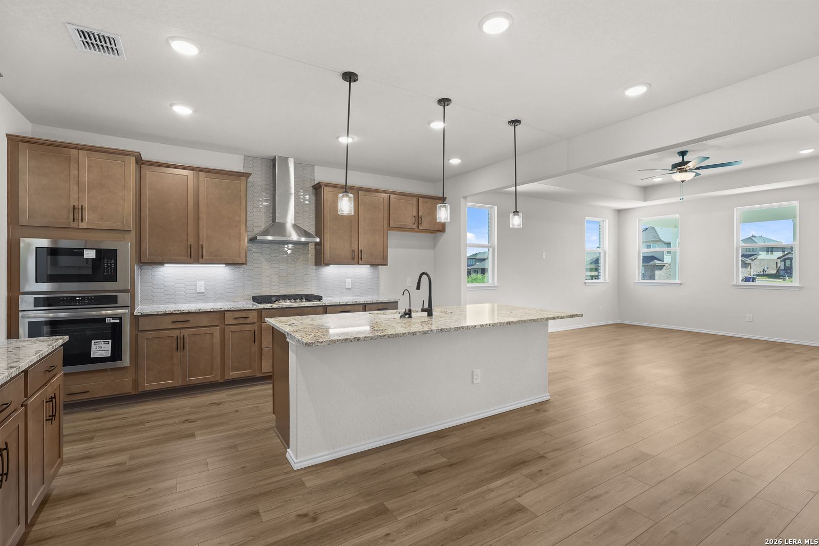 Open-concept kitchen with granite island, stainless appliances, and wood floors in Davidson Homes Glenwood E, San Antonio, TX