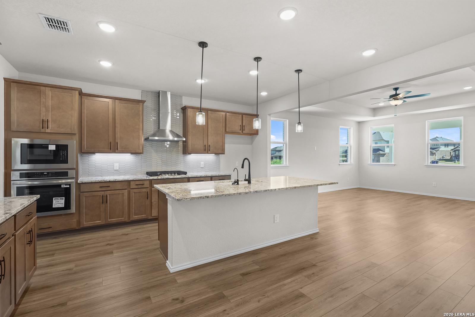Open-concept kitchen with granite island, stainless appliances, and wood floors in Davidson Homes Glenwood E, San Antonio, TX