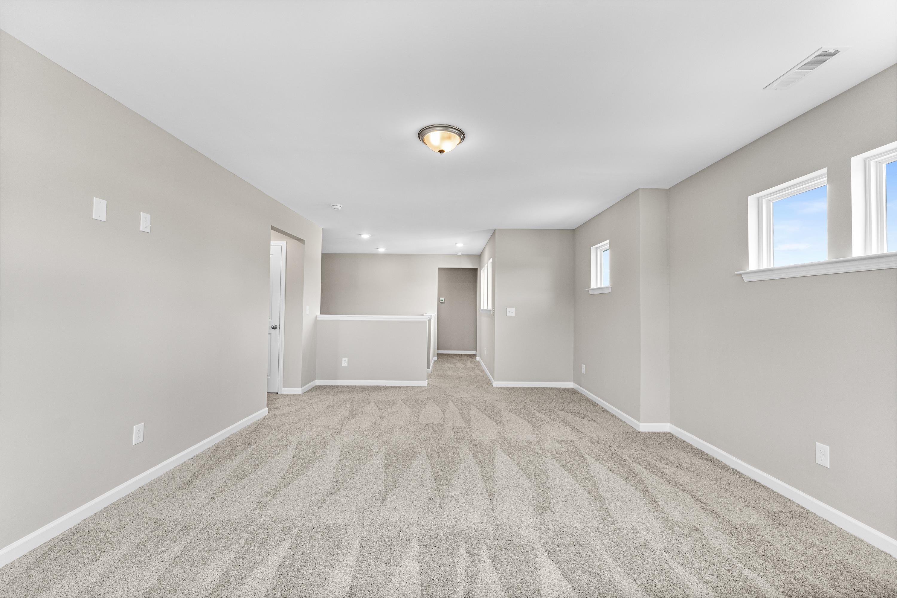 Spacious interior of The Haven E by Evermore Homes, Owens Cross Roads AL, featuring neutral beige walls, patterned carpet floor, large windows