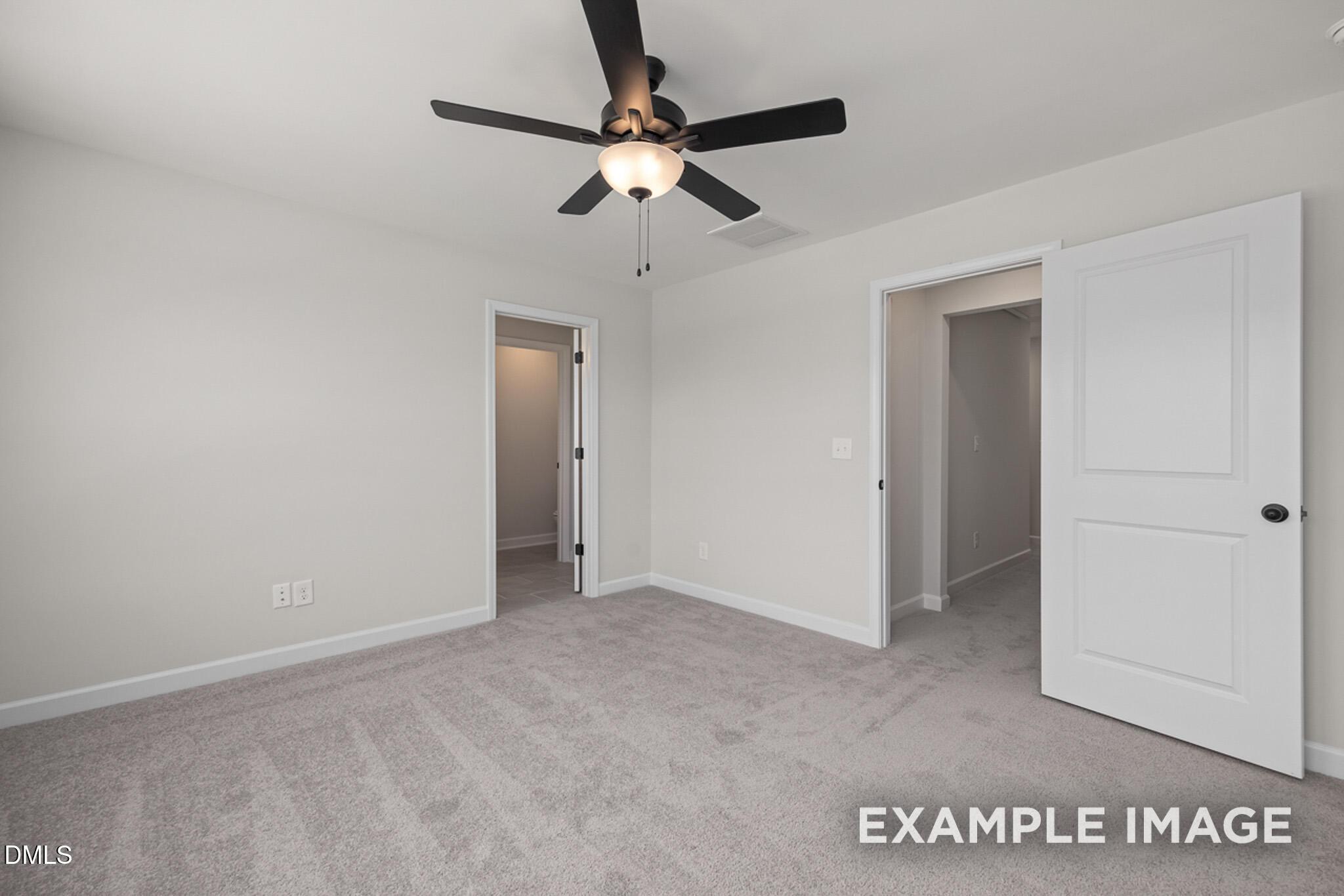 Spacious bedroom with gray carpeting, ceiling fan, and doorways in The Mitchell floor plan at Camden Park, Knightdale, NC.