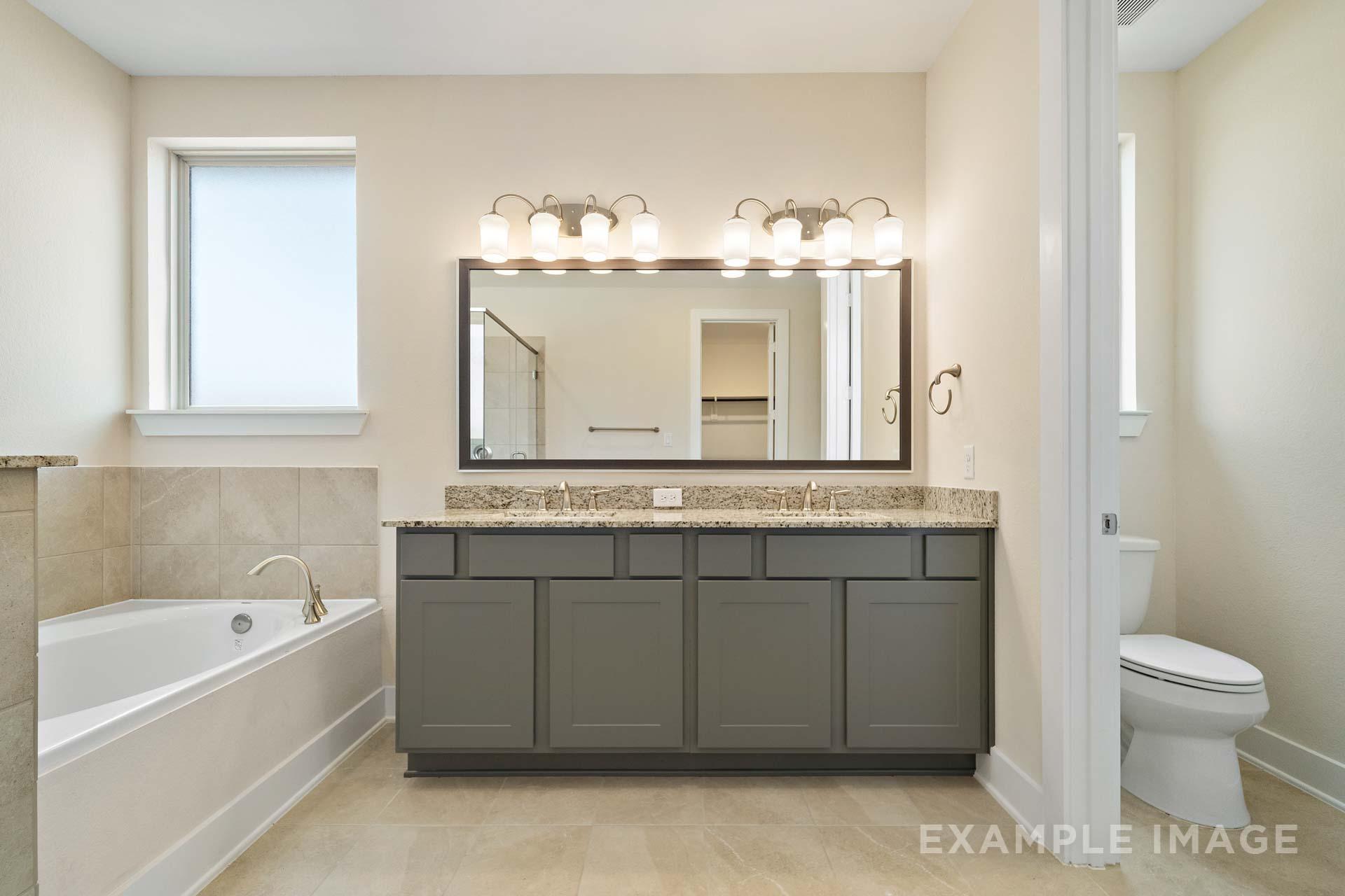 Spacious master bathroom in The Diana C with double sink vanity, soaking tub, and neutral tile accents