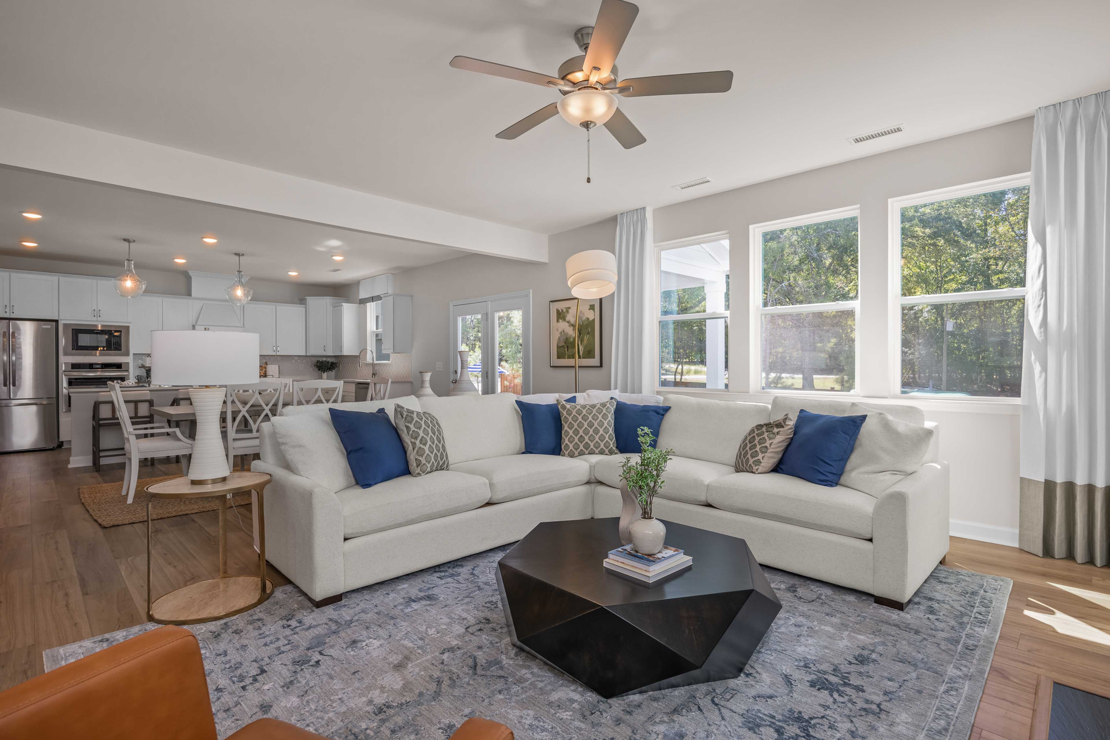 Spacious open-concept living room at Sage on North Main in Wake Forest NC with white L-shaped sofa, blue pillows, hardwood floors, modern kitchen