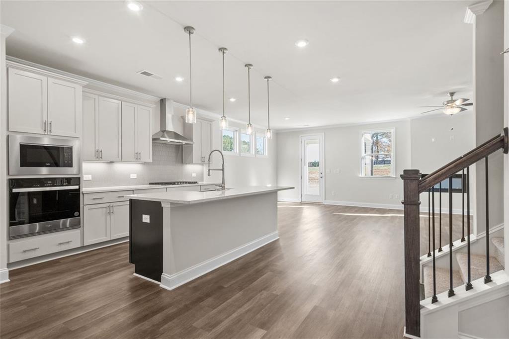 Modern open-concept kitchen with white cabinets, stainless steel appliances, large island sink, and hardwood floors in Davidson Homes The Ash C, Hoschton
