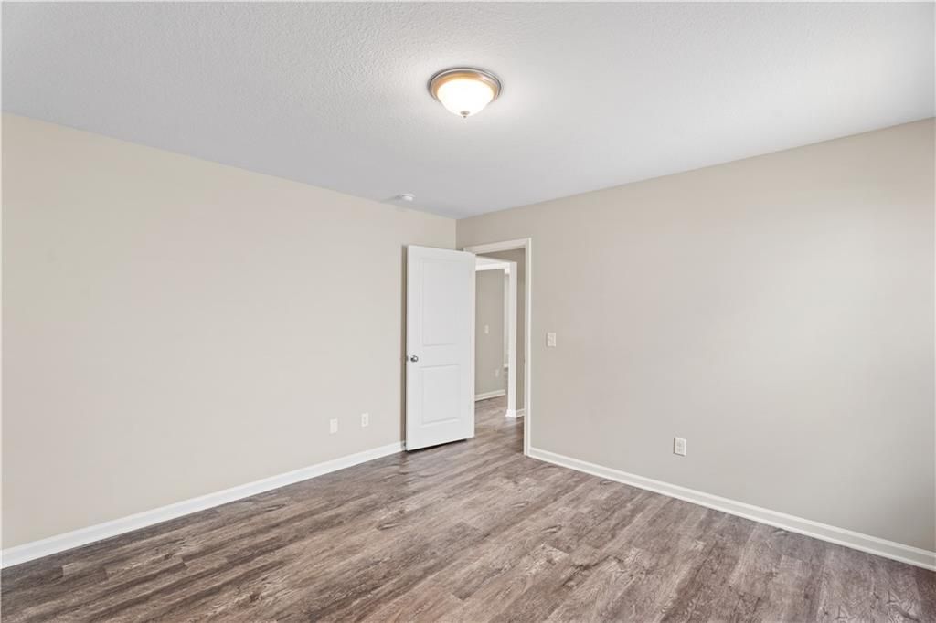 Empty secondary bedroom with beige walls, hardwood floors, white door, and adjacent bath entry in Davidson Homes The Washington, Phenix City, Alabama