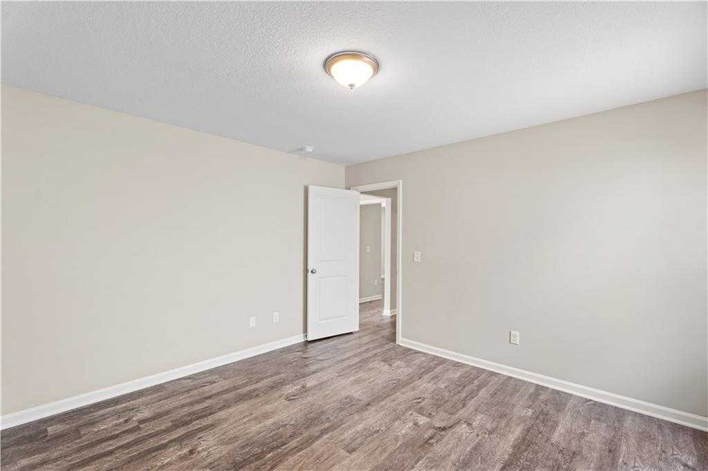 Empty secondary bedroom with beige walls, hardwood floors, white door, and adjacent bath entry in Davidson Homes The Washington, Phenix City, Alabama