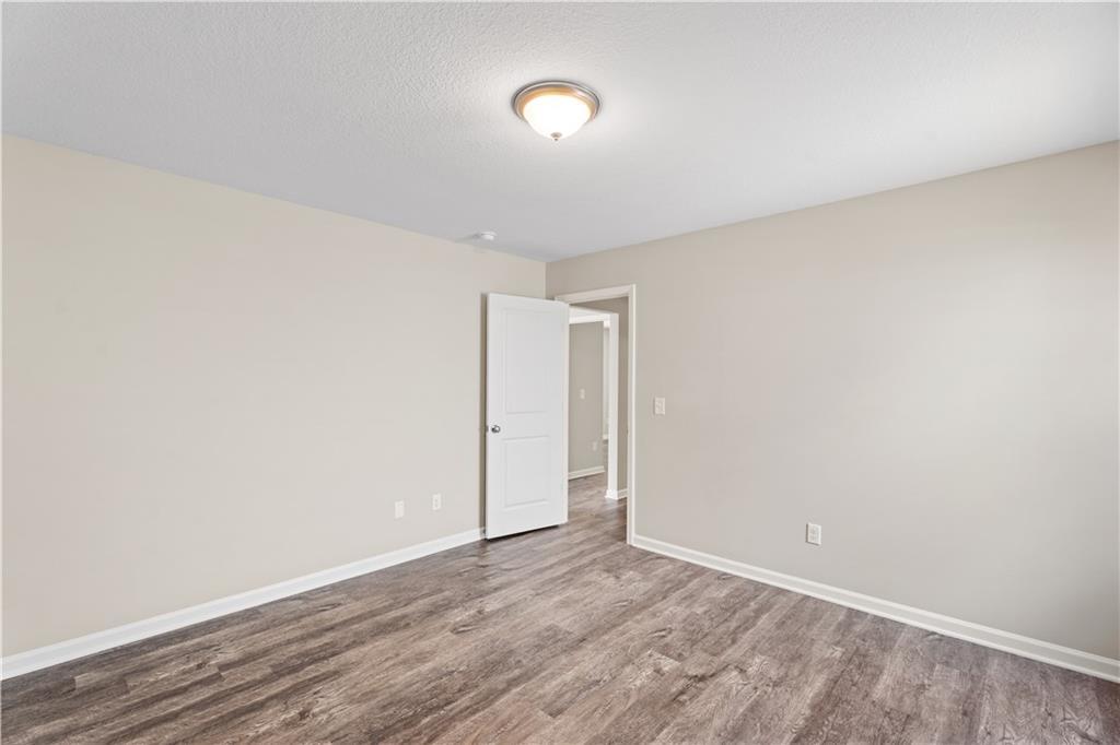 Empty secondary bedroom with beige walls, hardwood floors, white door, and adjacent bath entry in Davidson Homes The Washington, Phenix City, Alabama