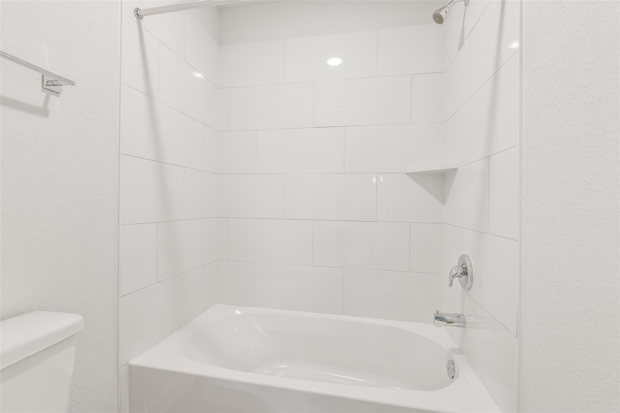 Modern white subway tile bathroom with glass shower, niche shelf, and freestanding tub in Davidson Homes The San Marcos E, Cleveland, Texas