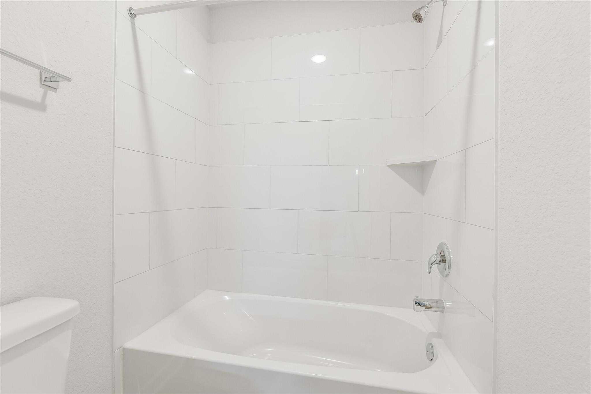 Modern white subway tile bathroom with glass shower, niche shelf, and freestanding tub in Davidson Homes The San Marcos E, Cleveland, Texas