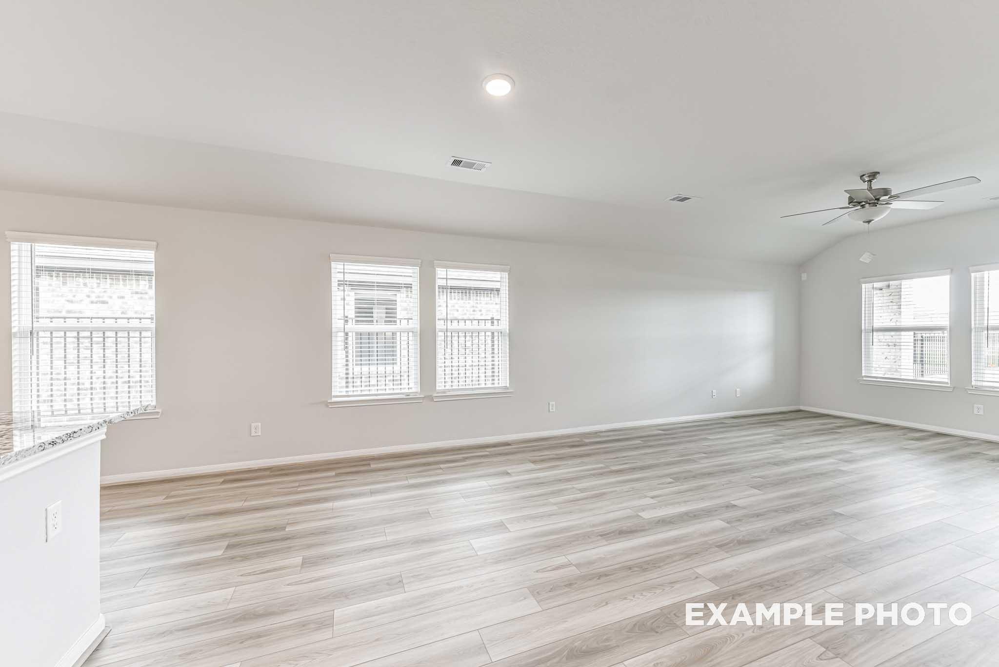 Spacious empty great room with light wood flooring, ceiling fan, large windows in Davidson Homes The Riviera A, Rosharon, Texas