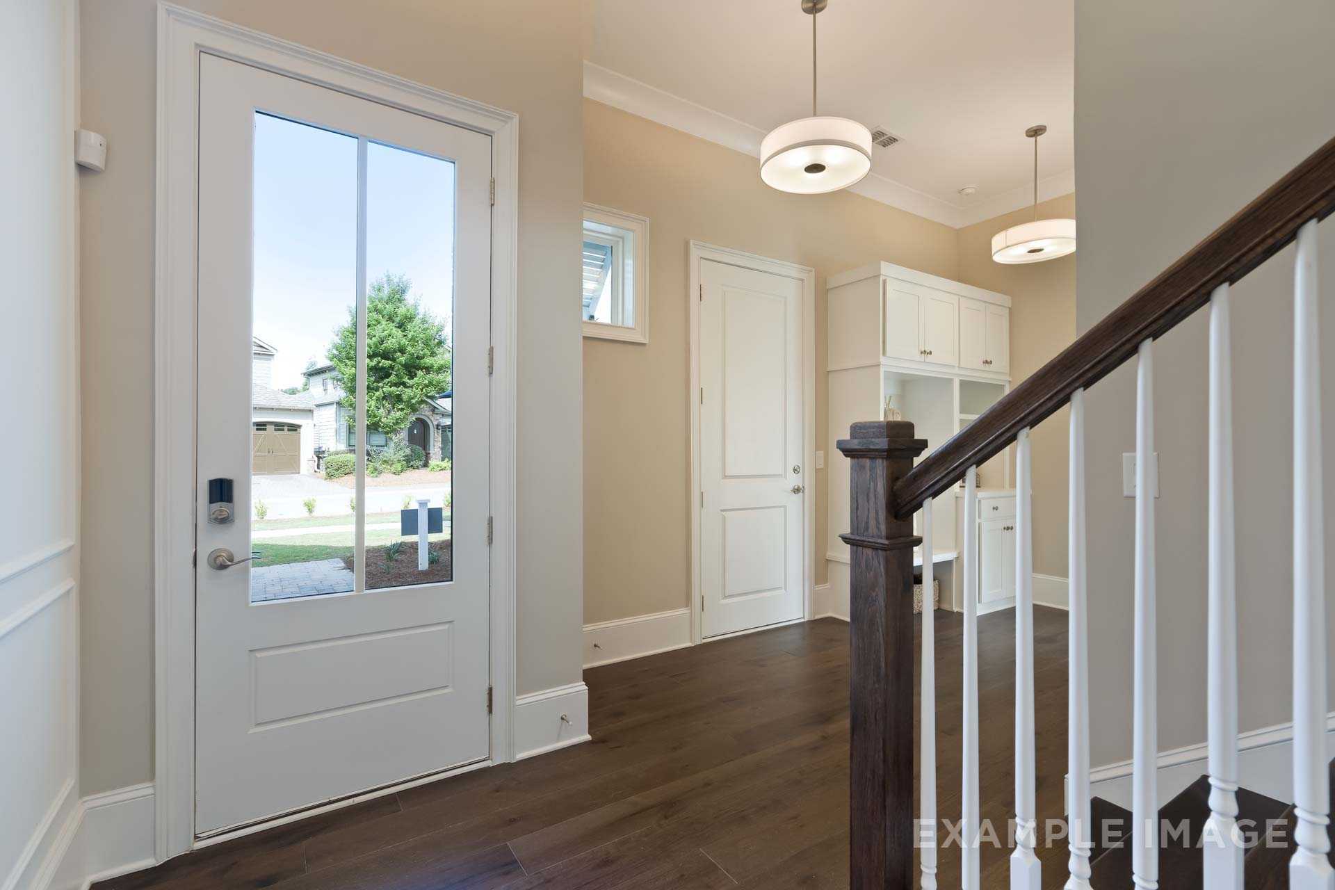 Spacious foyer in The Seaside B home design featuring dark hardwood floors, elegant wood staircase, and glass-paneled front door