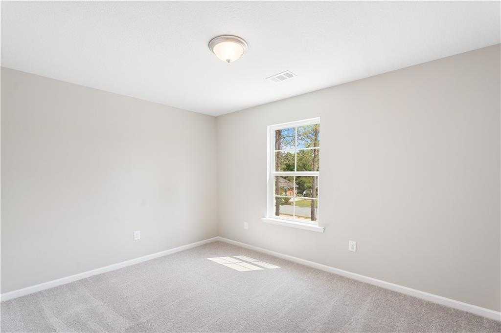Bright empty bedroom with light gray walls, plush carpet, and sunny window in Evermore Homes The Washington, Phenix City, Alabama