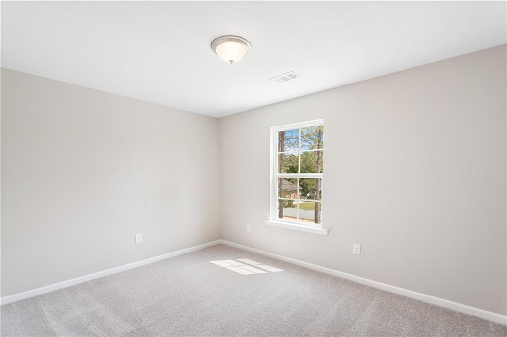 Bright empty bedroom with light gray walls, plush carpet, and sunny window in Evermore Homes The Washington, Phenix City, Alabama