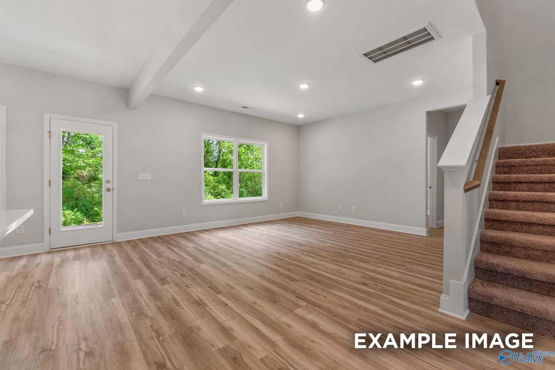 Spacious open living room with hardwood floors, large window and door to lush backyard, wooden staircase in Davidson Homes The Shelby C, Meridianville Alabama
