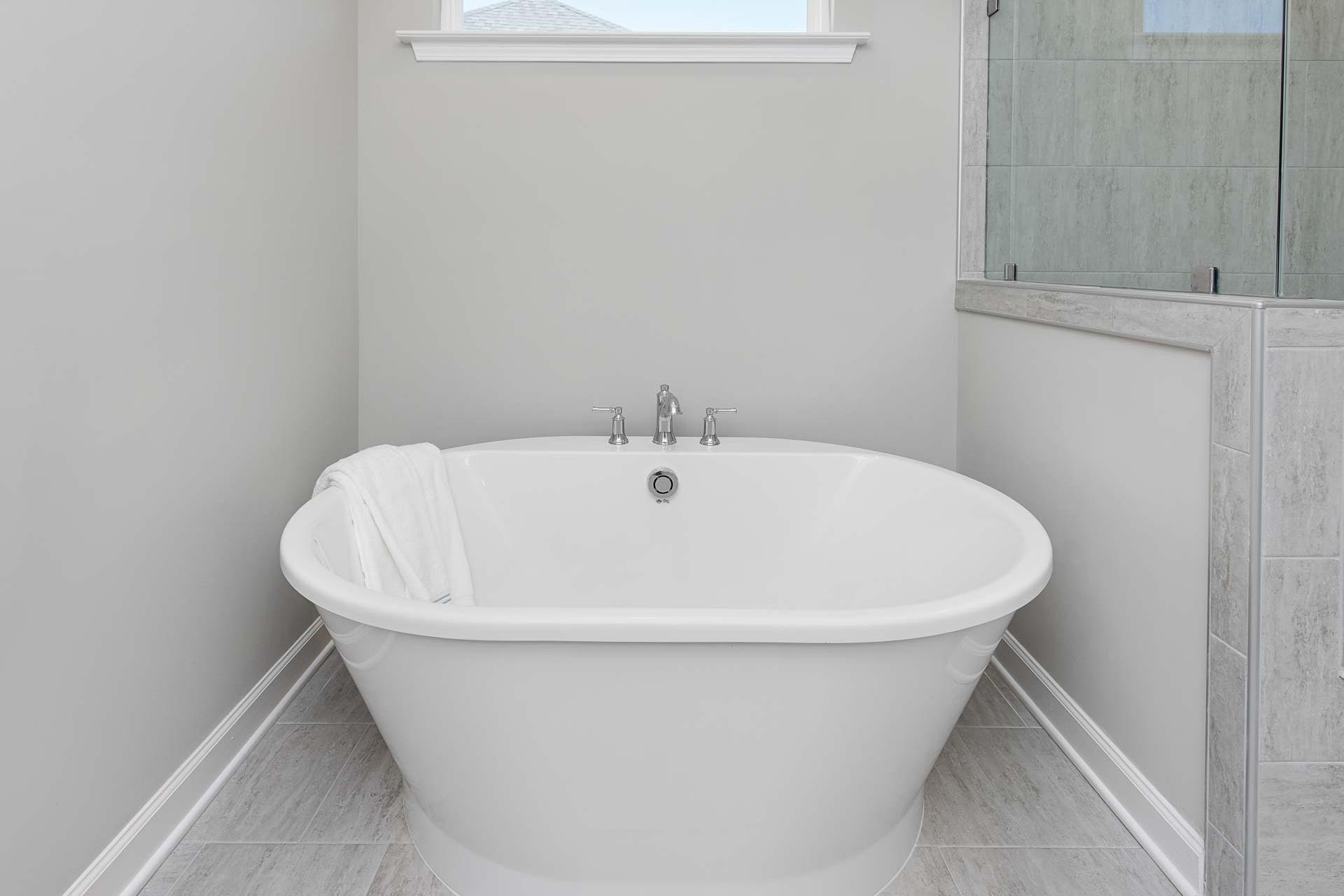 Freestanding oval bathtub in spacious bathroom at Highland Forest Fuquay-Varina NC with draped towel and glass shower