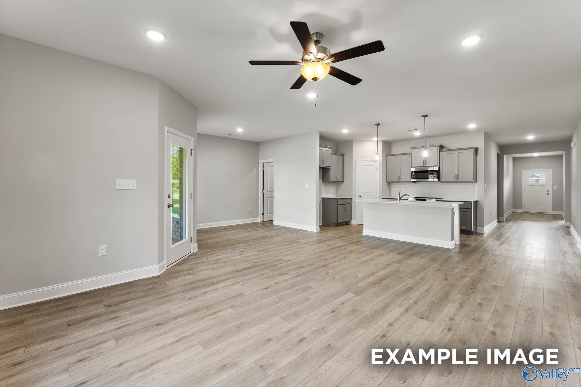 Open-concept living-kitchen with hardwood floors, white cabinets, stainless appliances and ceiling fan in The Daphne F 4-bedroom home, Hazel Green, Alabama