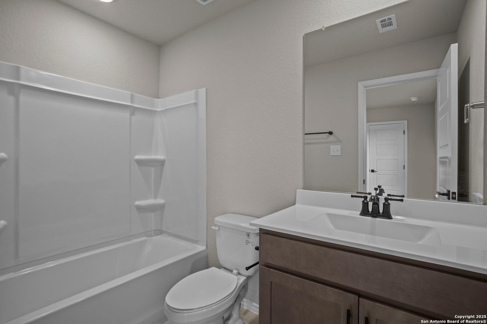 Modern guest bathroom with tub-shower combo, single vanity sink, mirror, and neutral walls in Davidson Homes The Douglas F, San Antonio