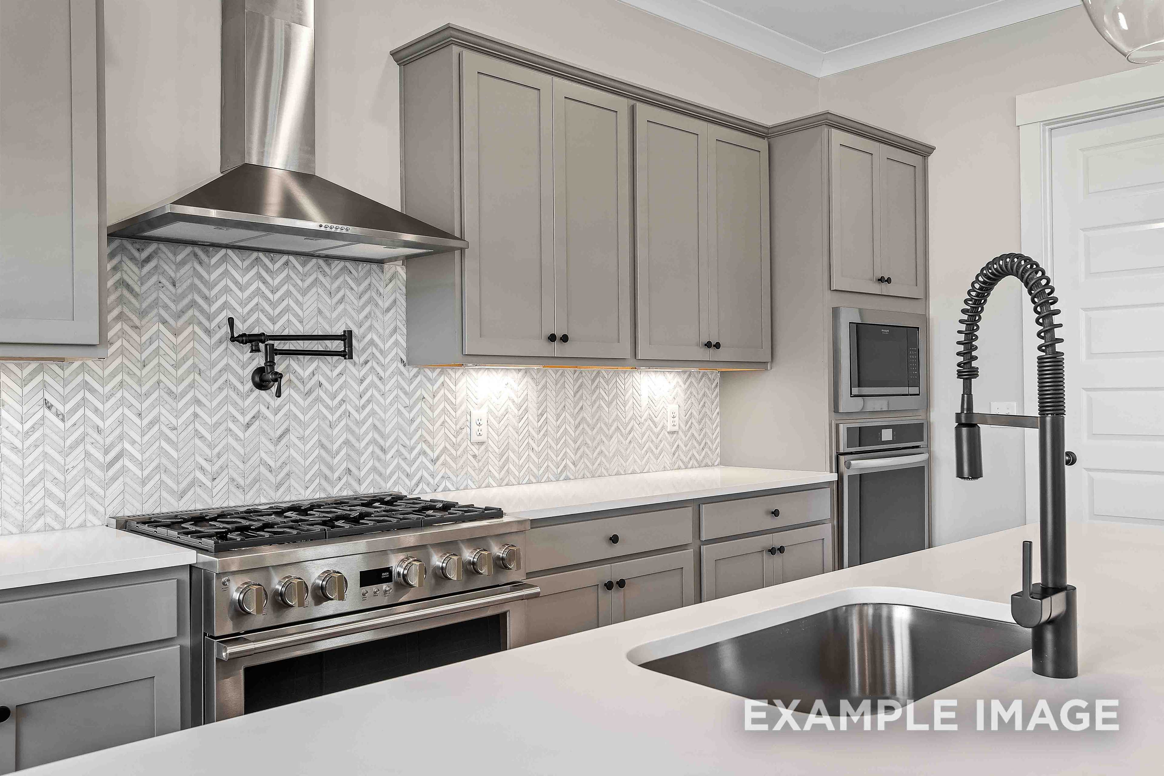 Modern Alston A kitchen with gray shaker cabinets, herringbone marble backsplash, stainless steel gas range, and pull-down faucet sink