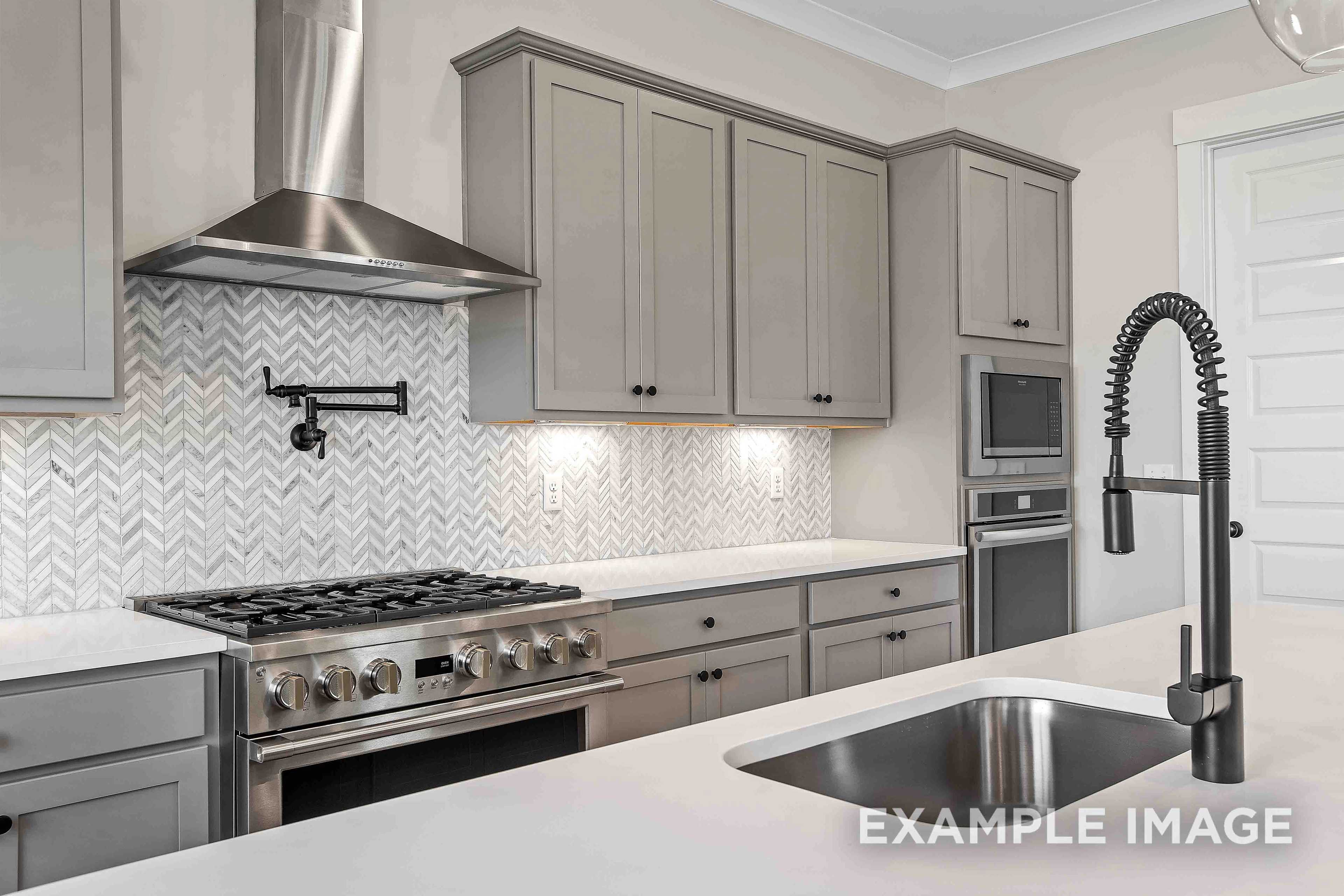 Modern Alston A kitchen with gray shaker cabinets, herringbone marble backsplash, stainless steel gas range, and pull-down faucet sink