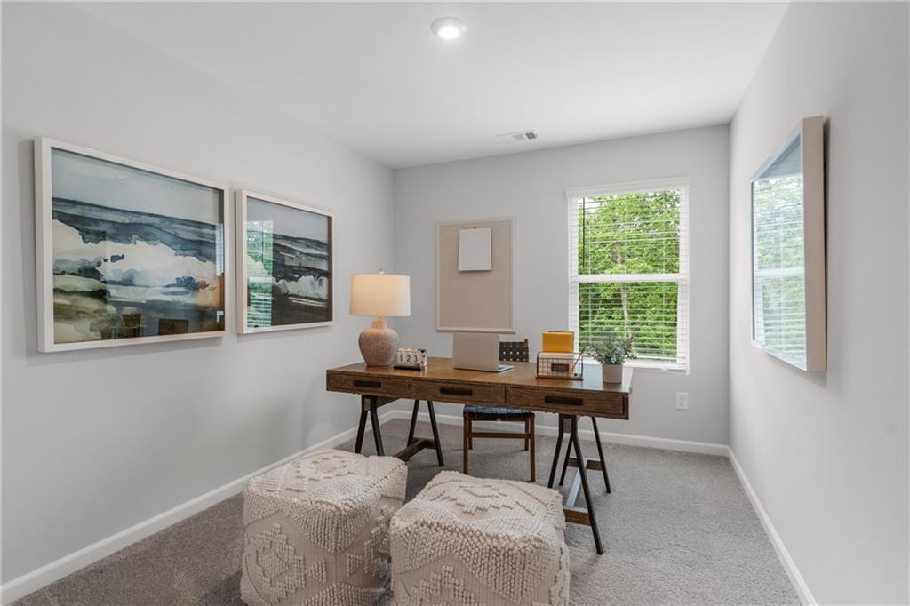 Cozy home office with wooden sawhorse desk, laptop, abstract ocean art, bulletin board, and tree-view window in Davidson Homes The Durant A, Emerson, GA
