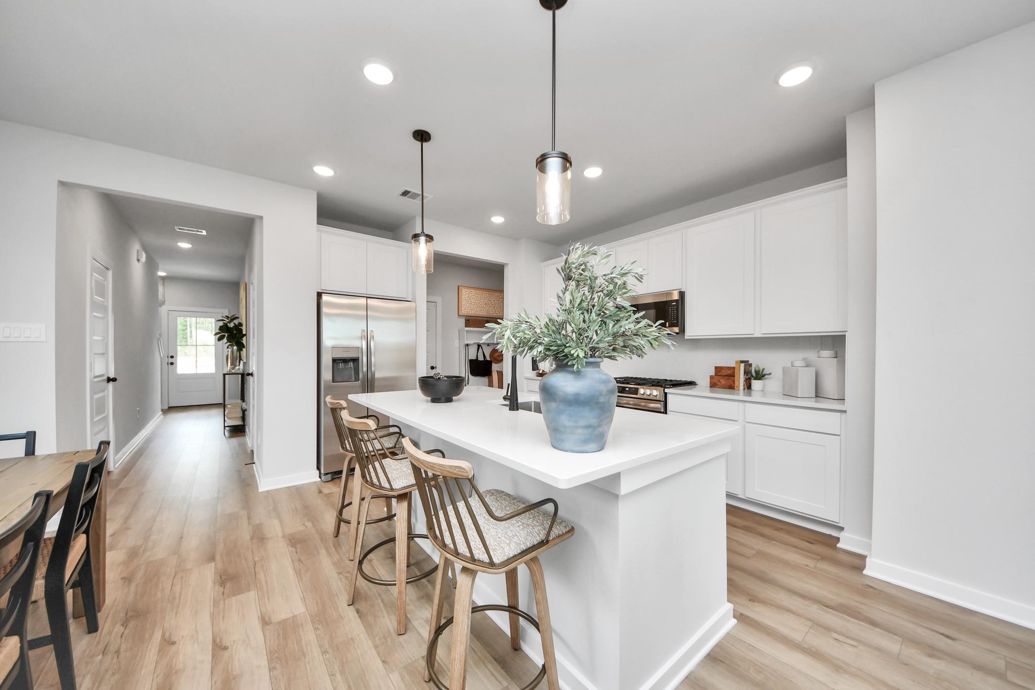 Modern kitchen with white cabinets, quartz island, and wood flooring at Robins Landing in Houston by Davidson Homes.