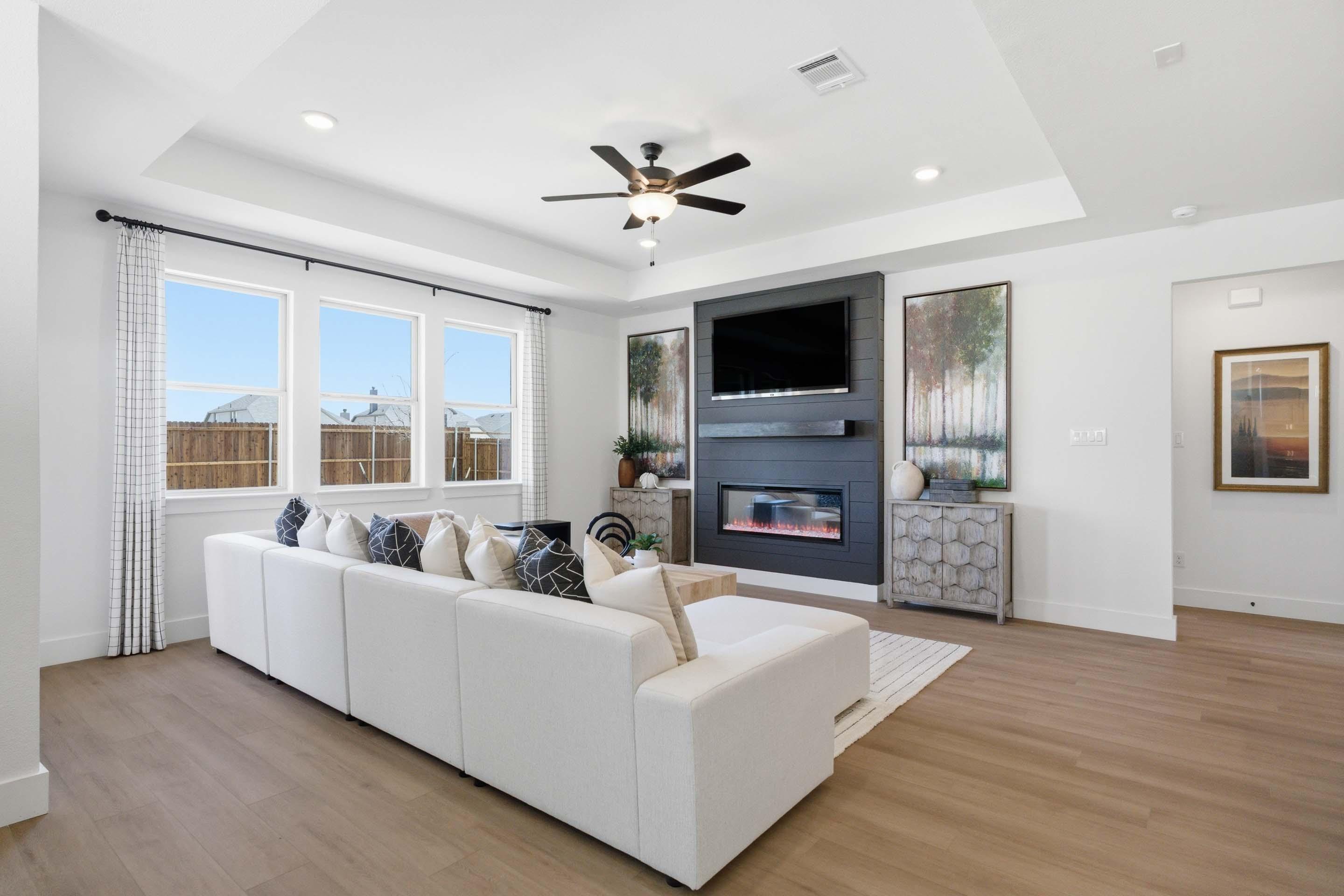 Bright, open-concept living room in The Laurel M featuring a modern fireplace, tray ceiling, and spacious sectional sofa.