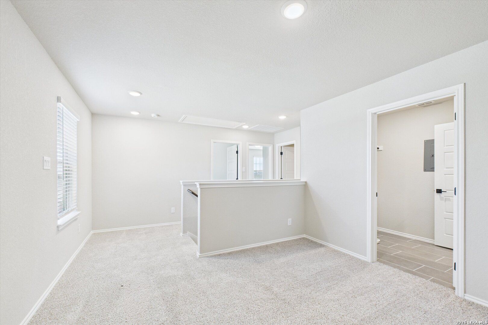 Bright upstairs hallway with white walls, beige carpet, recessed lights, and bedroom doors in Davidson Homes Charlotte A, San Antonio